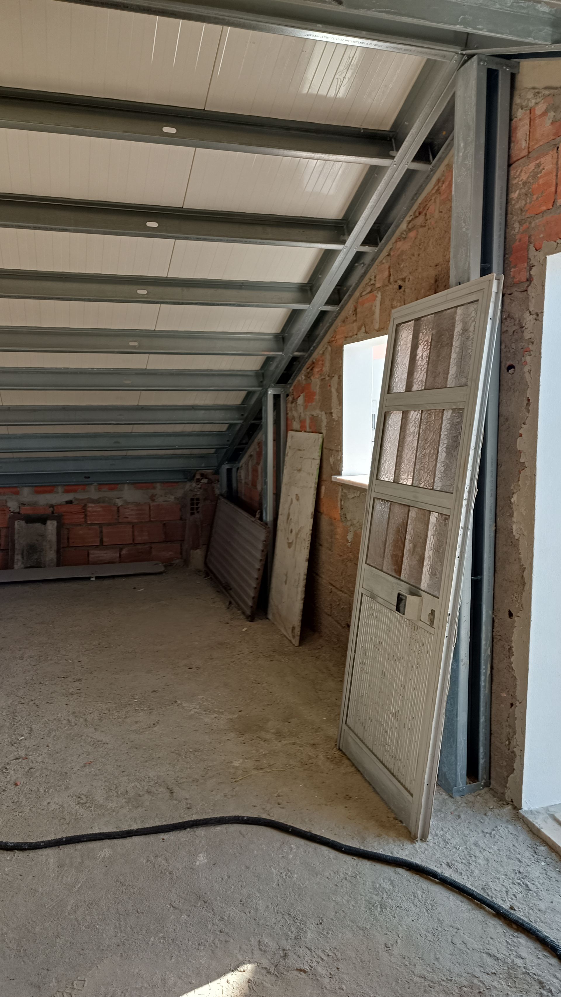Interior de um canteiro de obras: paredes nuas, vigas de metal e uma porta encostada na parede.