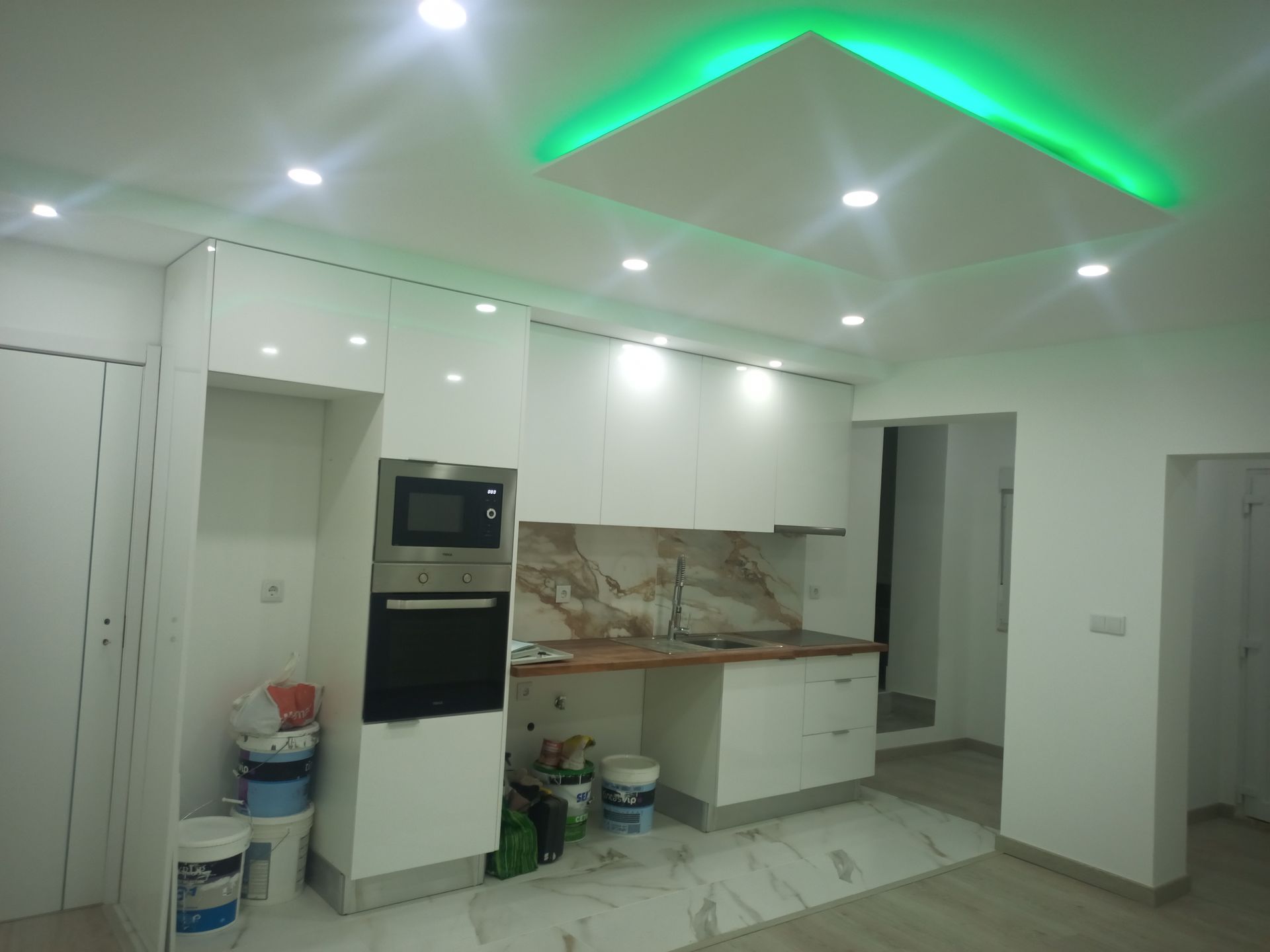 Cozinha branca com armários, eletrodomésticos embutidos e iluminação verde no teto.