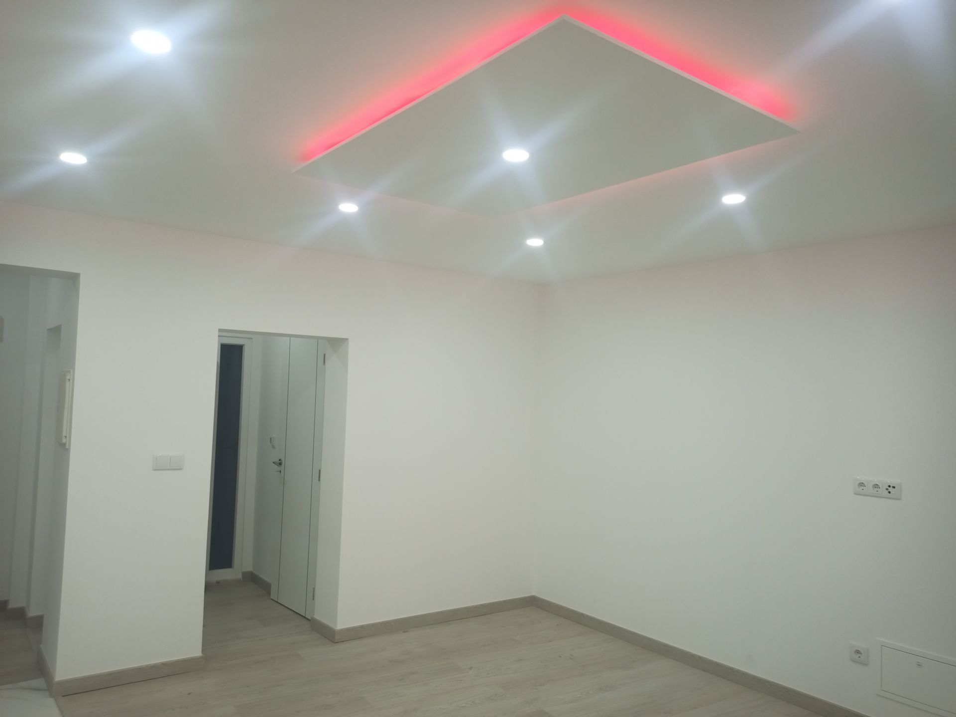 Sala branca e vazia com luzes embutidas no teto e um design quadrado com iluminação de destaque em vermelho.
