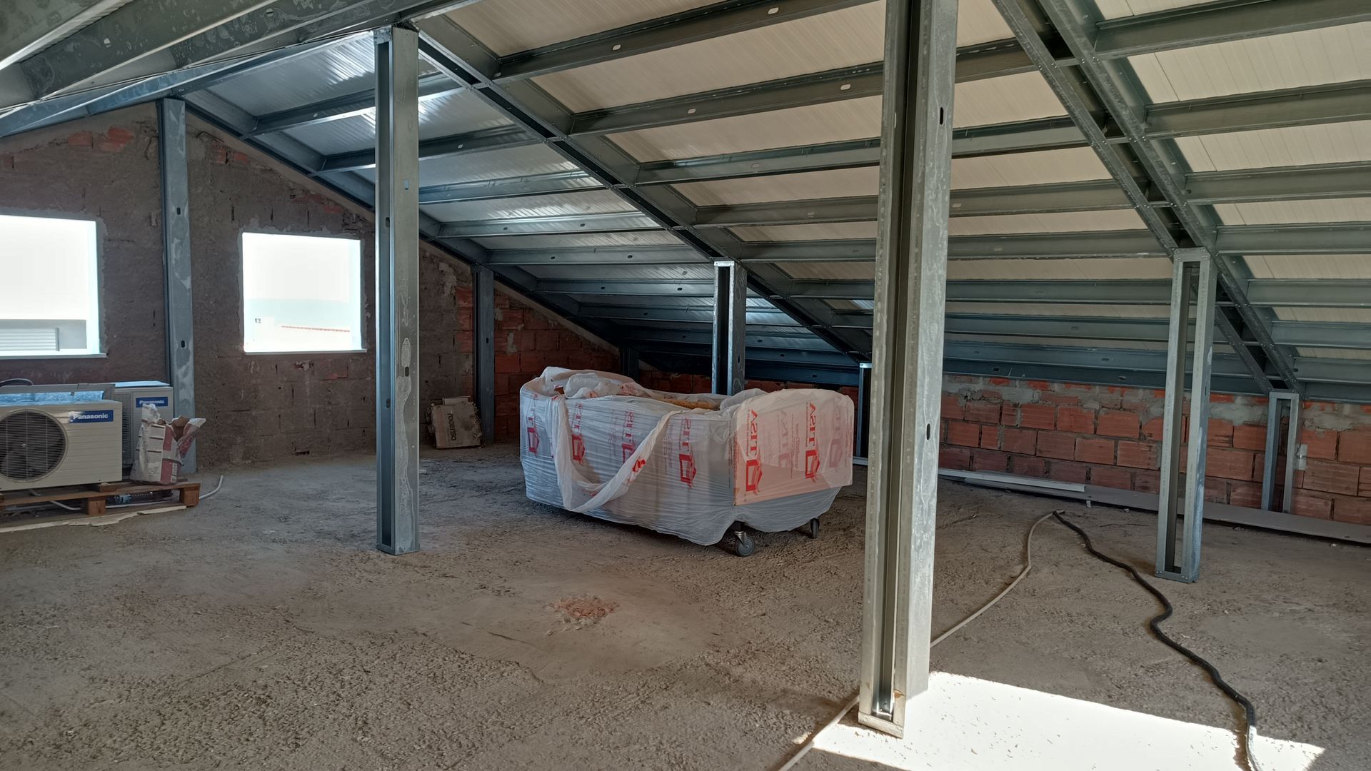 Interior de um sótão inacabado com estruturas metálicas de suporte e paredes de tijolo aparente.