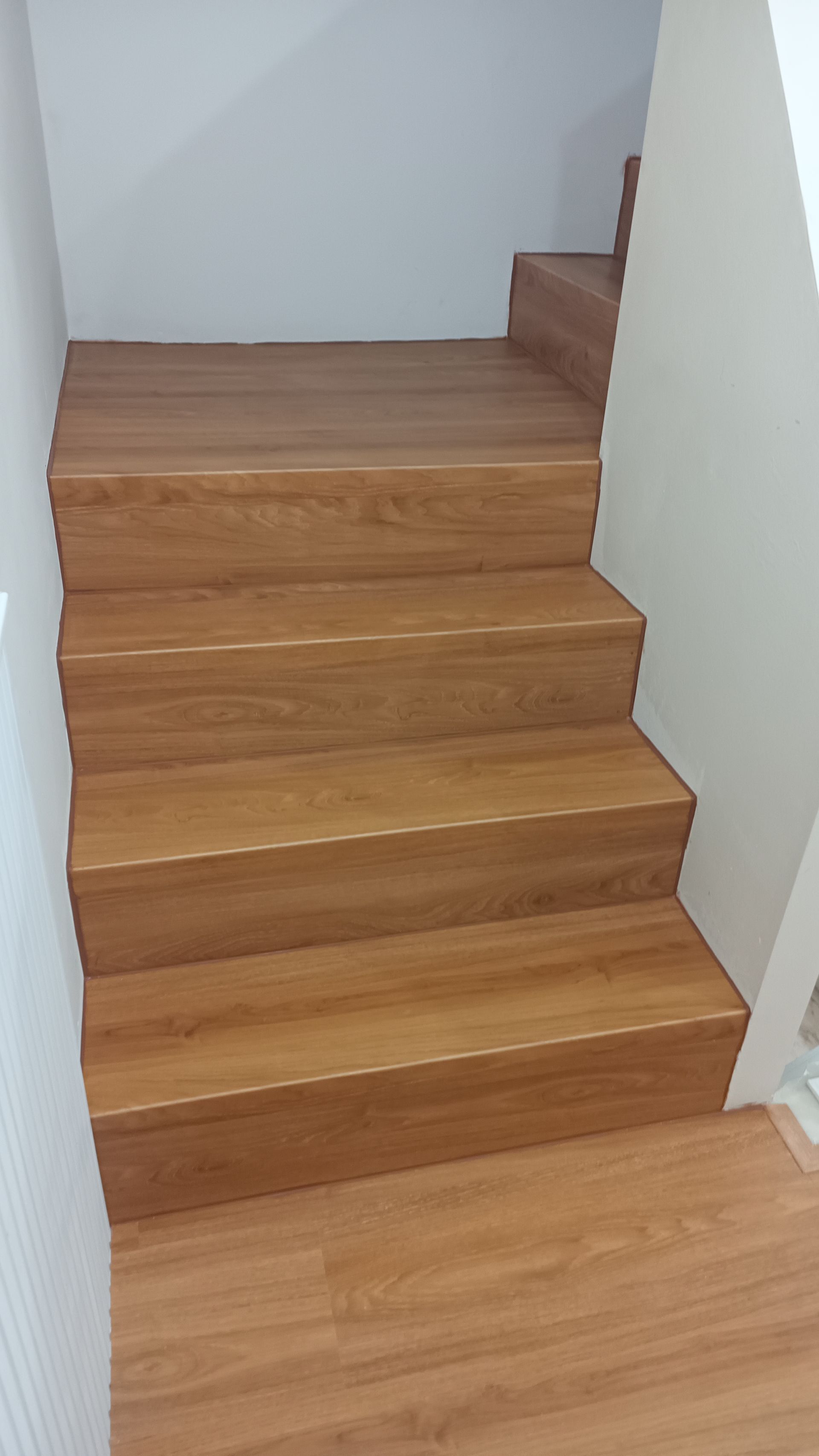 Escada de madeira que sobe, degraus e espelhos marrons, paredes brancas nas laterais.