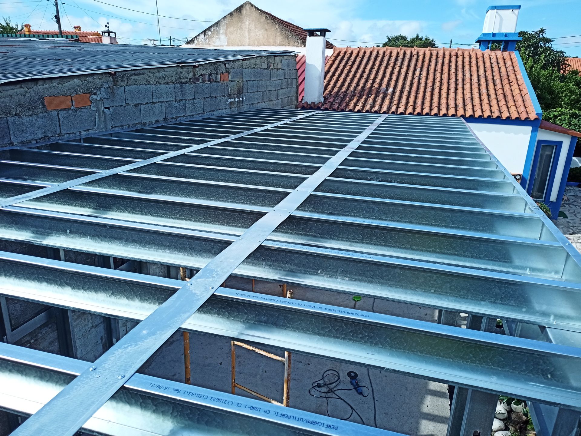 Instalação de estrutura metálica no telhado; vista externa do telhado de um edifício, com luz natural.