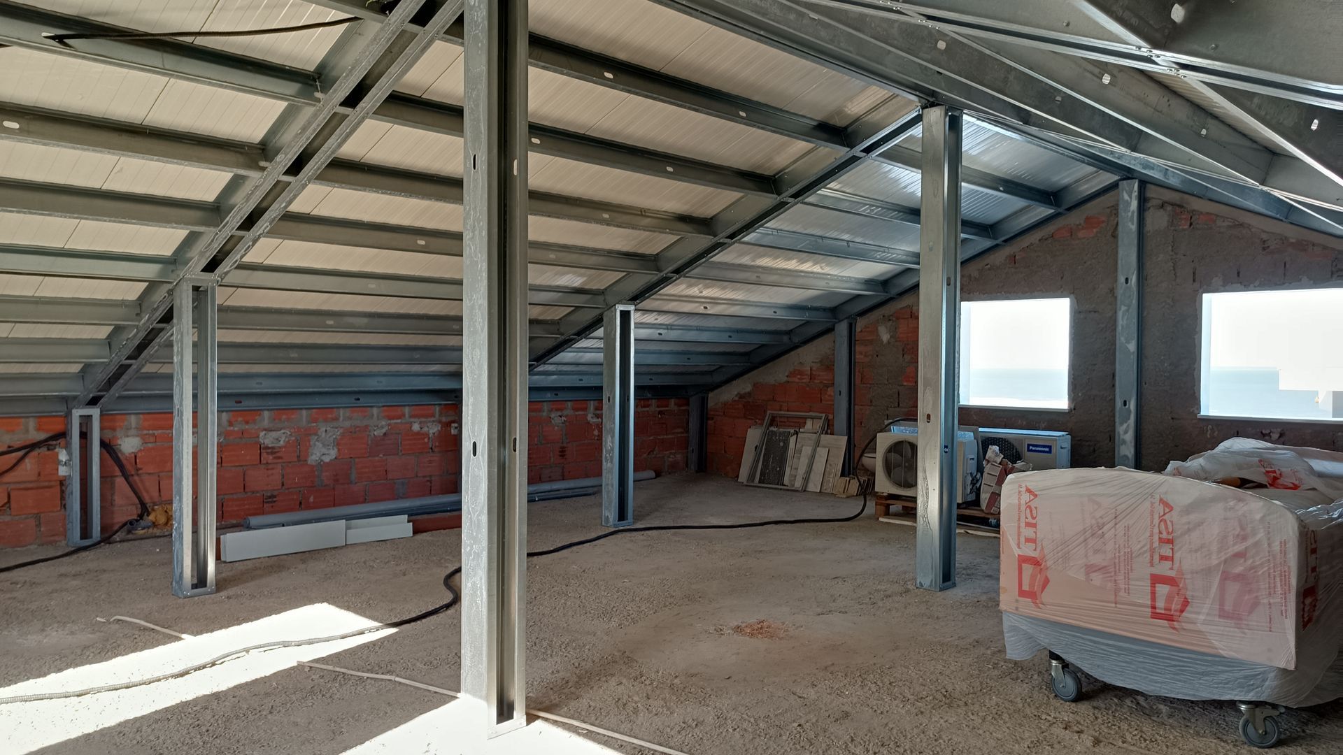 Interior de um edifício em construção, com vigas metálicas e paredes inacabadas visíveis.