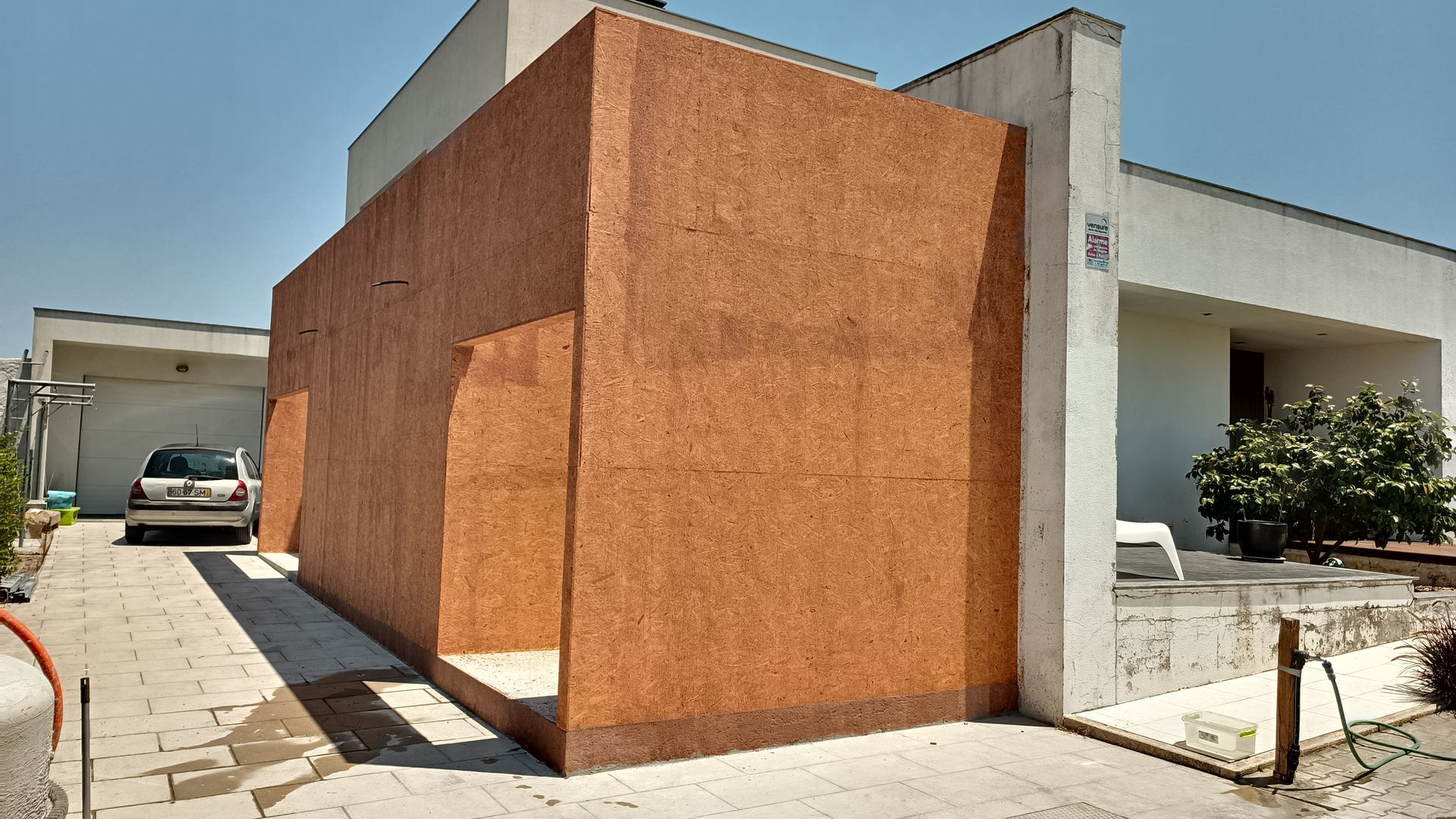 Uma estrutura de madeira marrom em frente a um prédio branco com um carro estacionado na entrada.