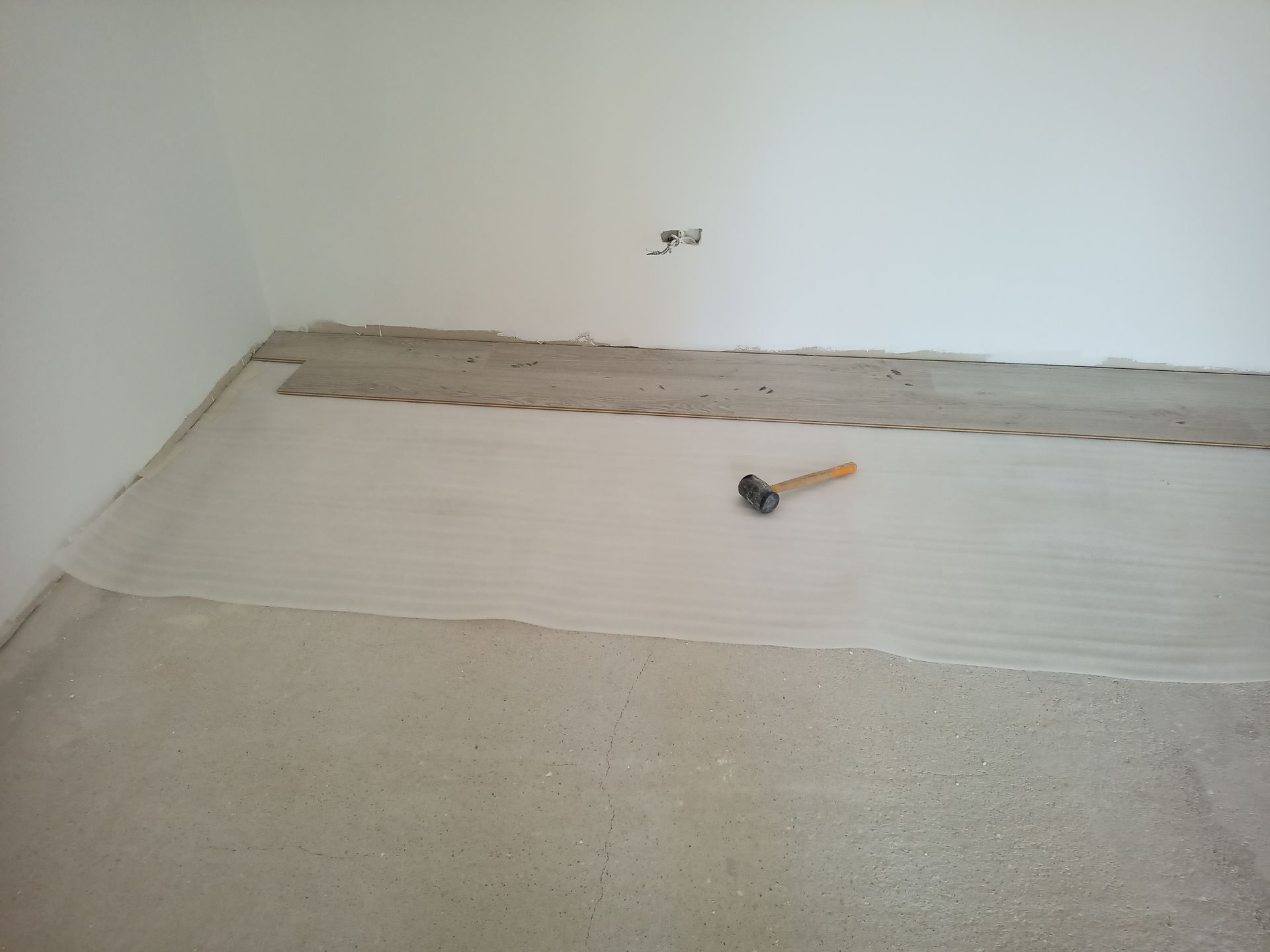 Piso com adesivo aplicado, pronto para receber o revestimento. Um martelo está apoiado sobre o adesivo. Parede branca ao fundo.