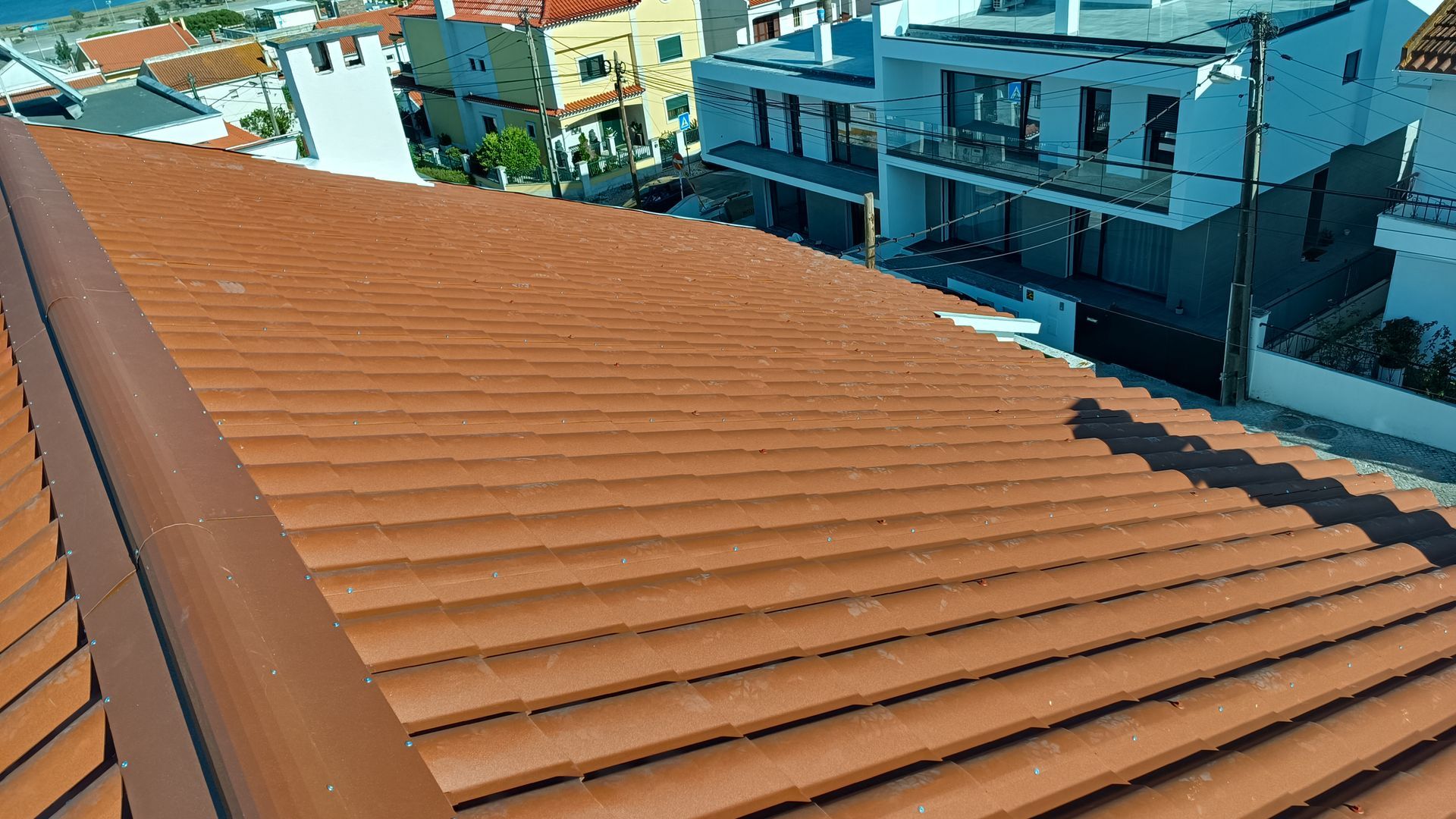 Telhado de telhas de terracota com detalhes em marrom escuro, com vista para um bairro de prédios brancos.