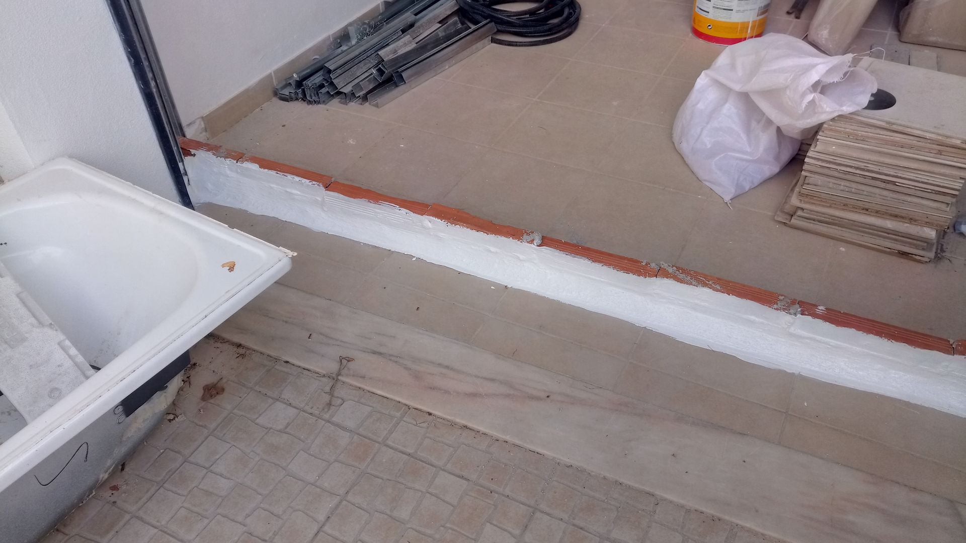 Banheiro em construção com banheira, tijolos aparentes e materiais de construção.