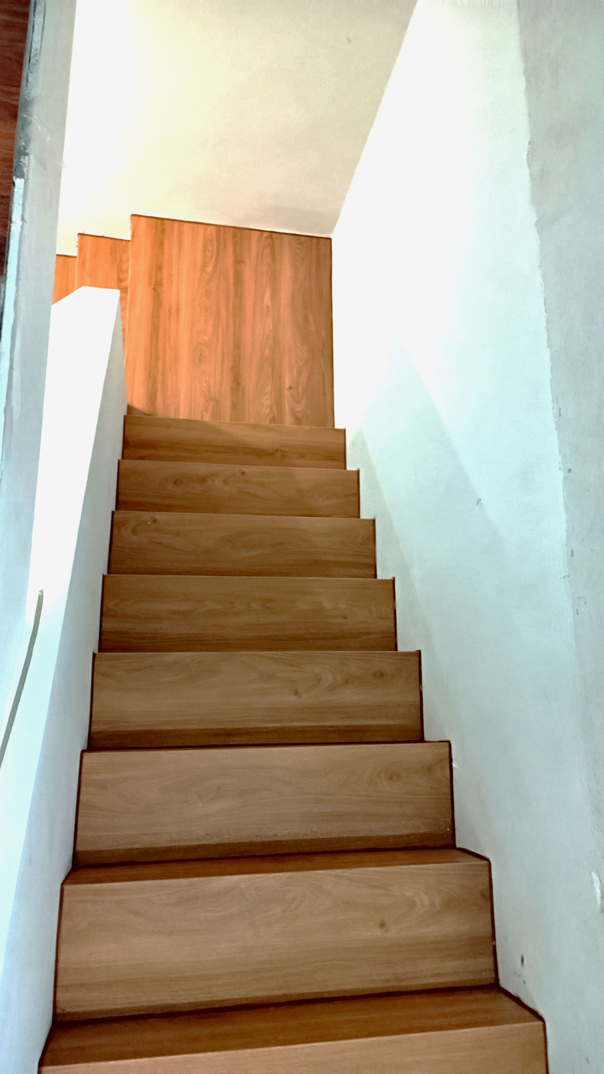 Escada de madeira que sobe entre paredes brancas; luz natural.