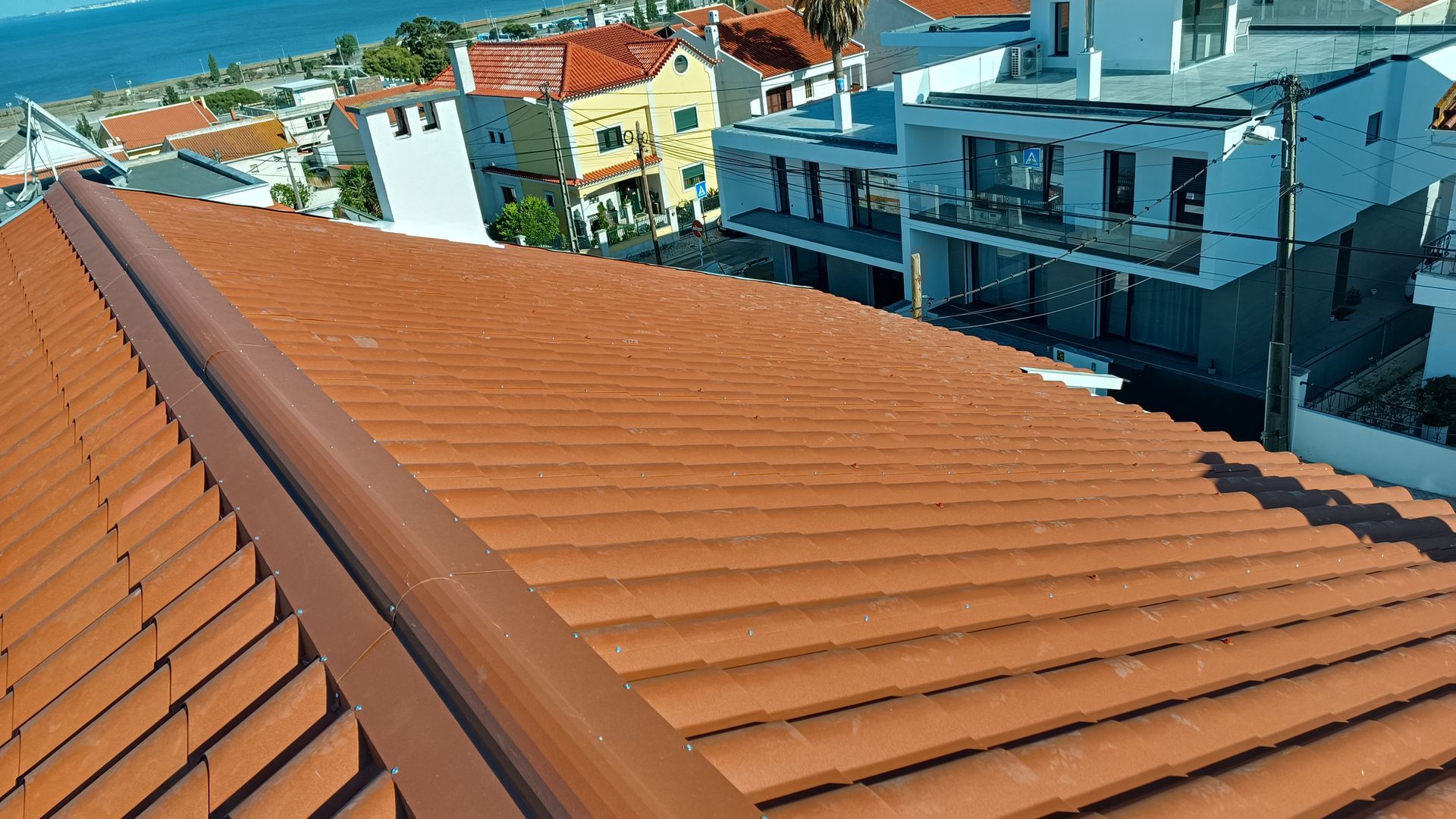 Close-up de um telhado de telhas vermelhas com borda marrom, com vista para edifícios e um corpo d'água.