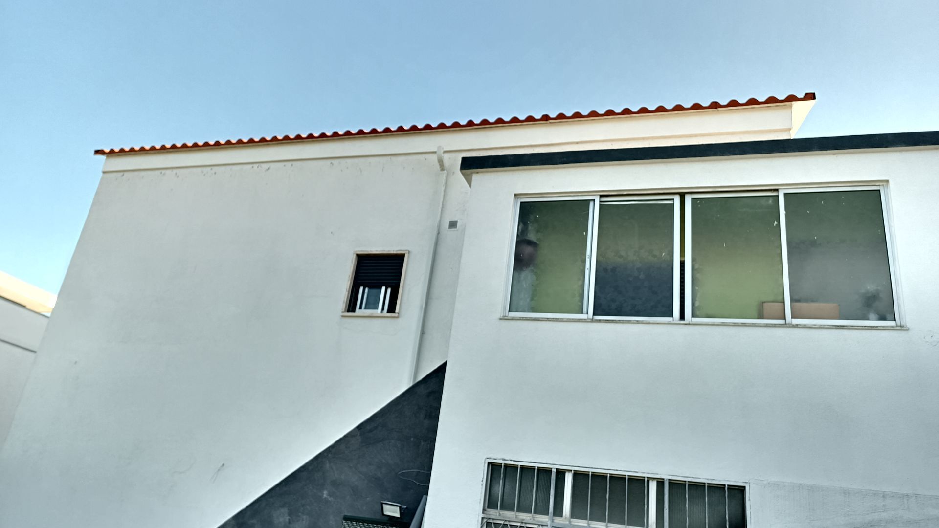 Exterior de prédio branco com janelas, telhas vermelhas e céu azul.