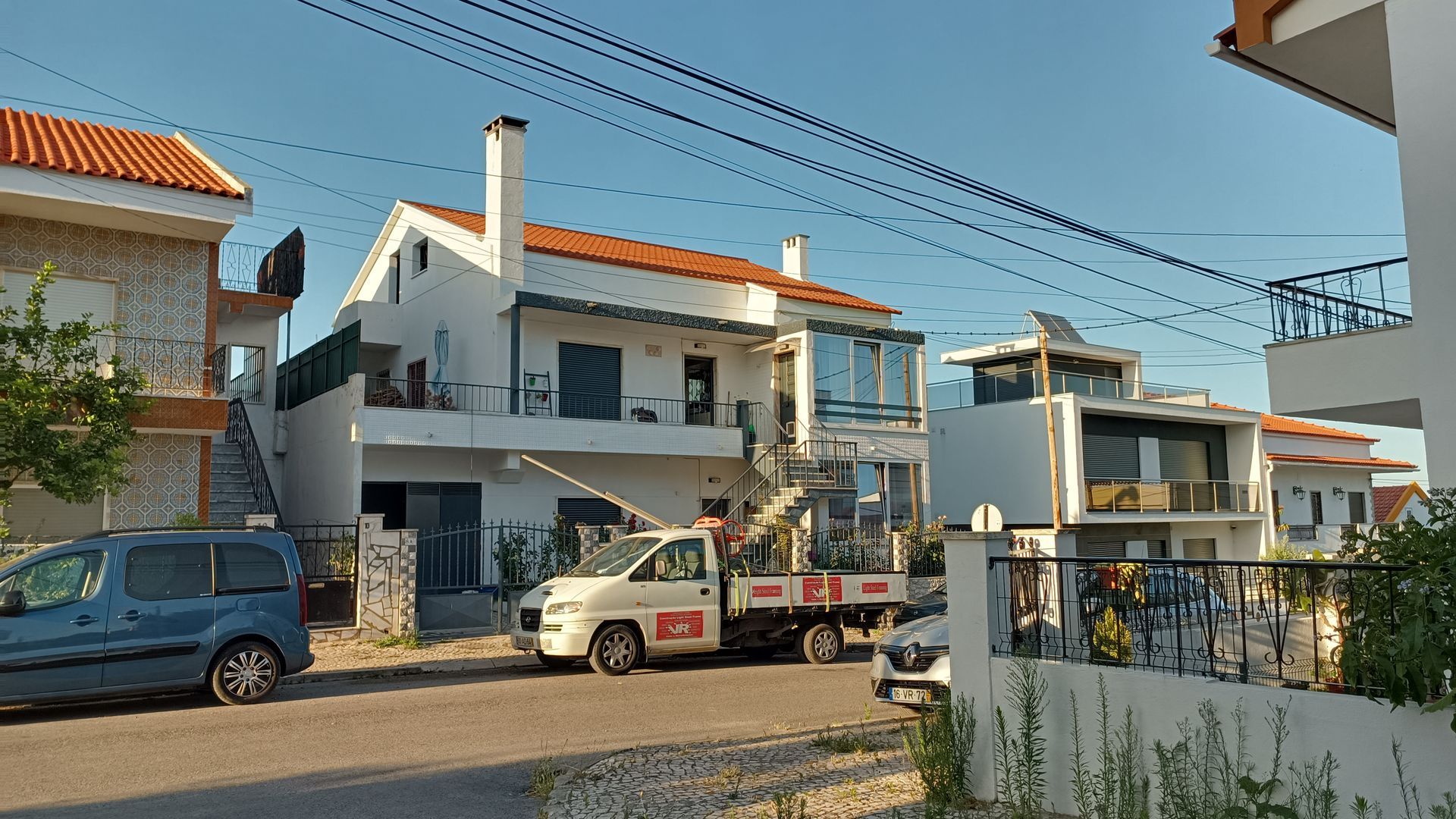 Casas numa rua, uma caminhonete branca estacionada na frente. Céu azul.