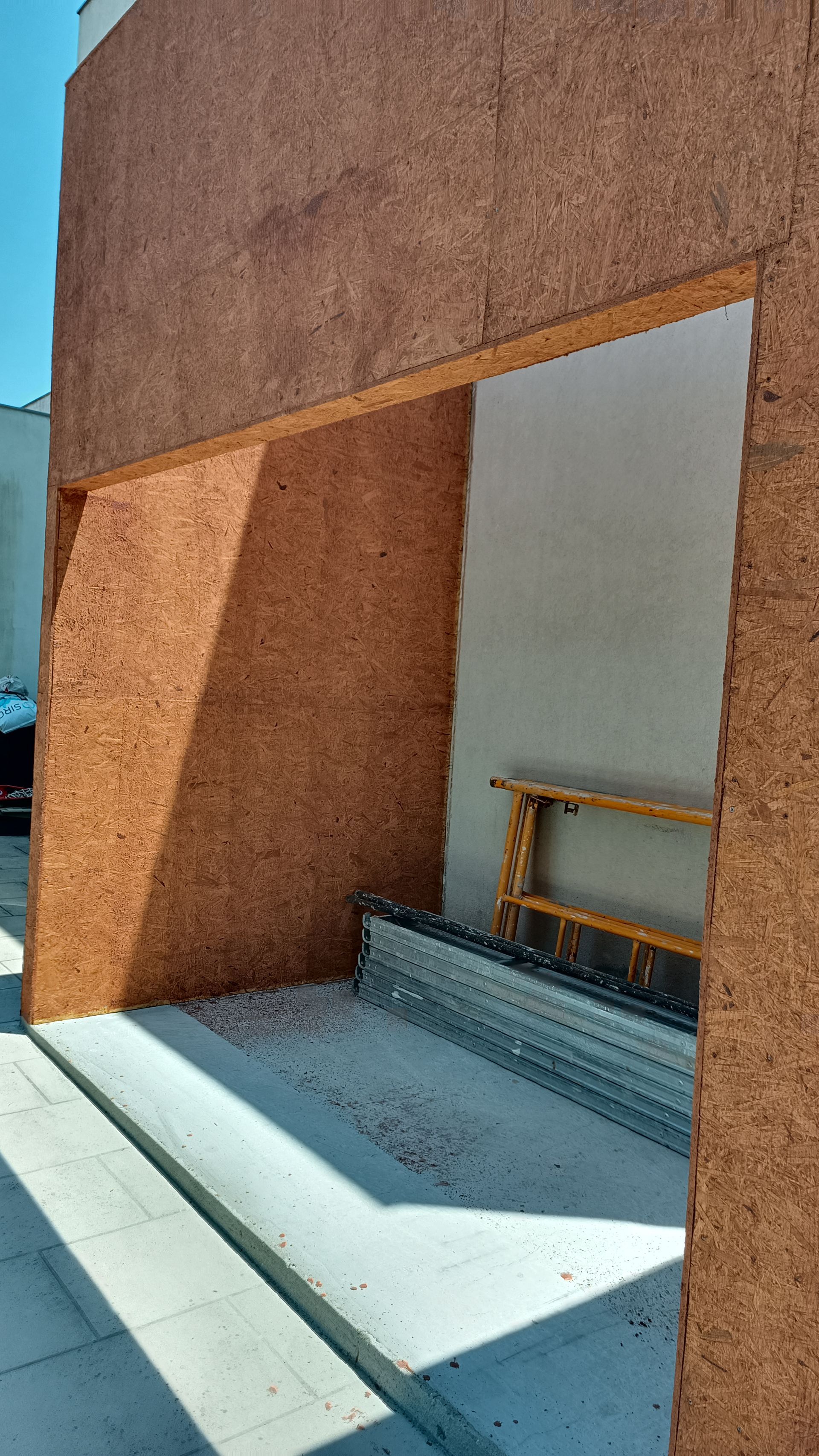 Canteiro de obras com uma porta emoldurada em madeira marrom e uma rampa de concreto.