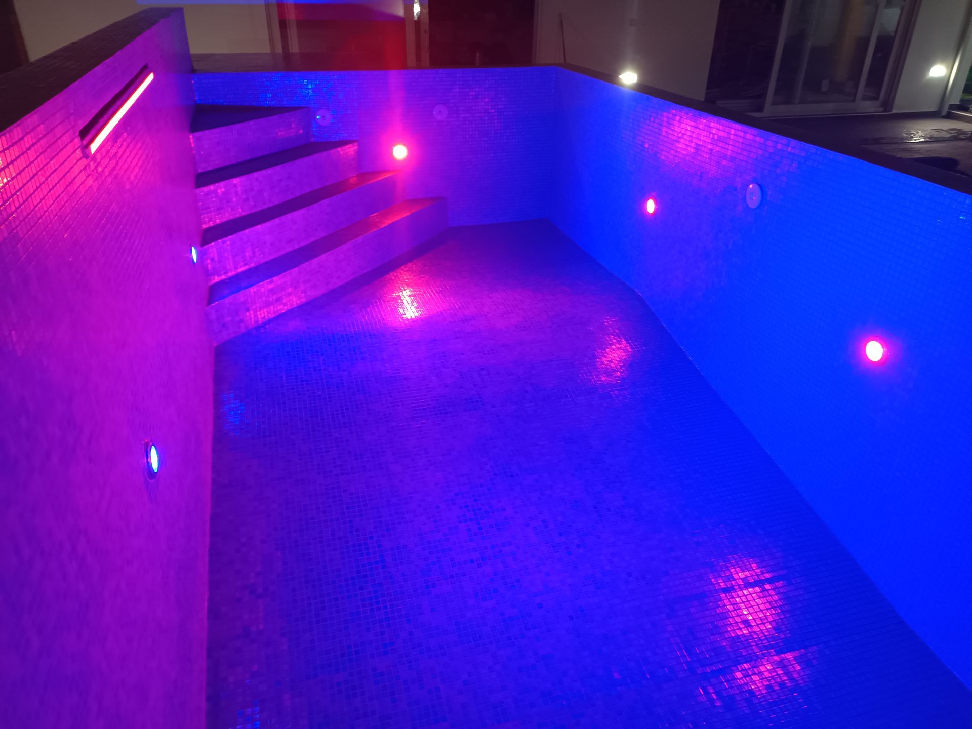 Piscina iluminada com degraus e luzes azuis e roxas.