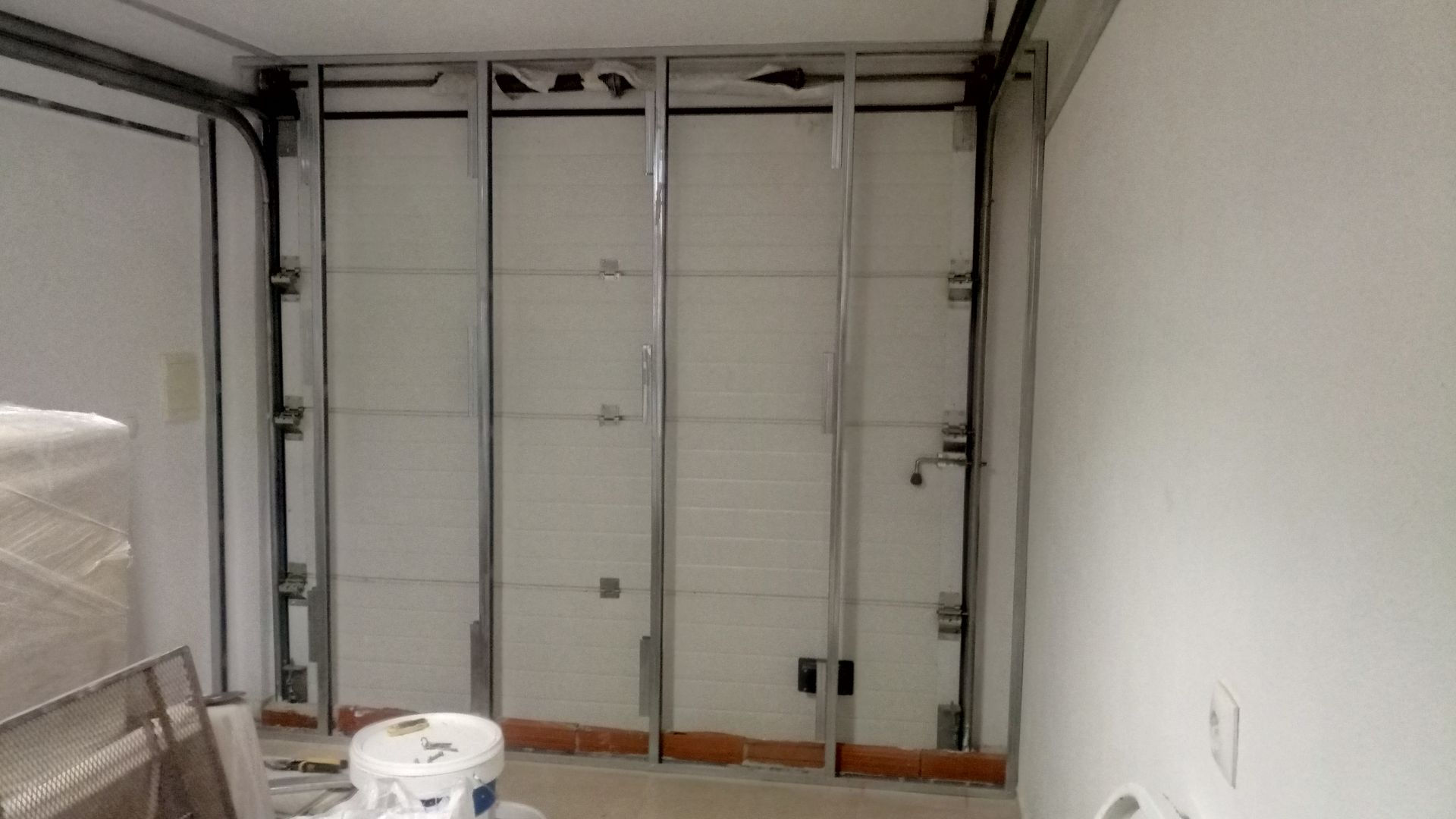 Vista interna de uma porta de garagem com estrutura metálica. Painéis de porta brancos, em um canteiro de obras.