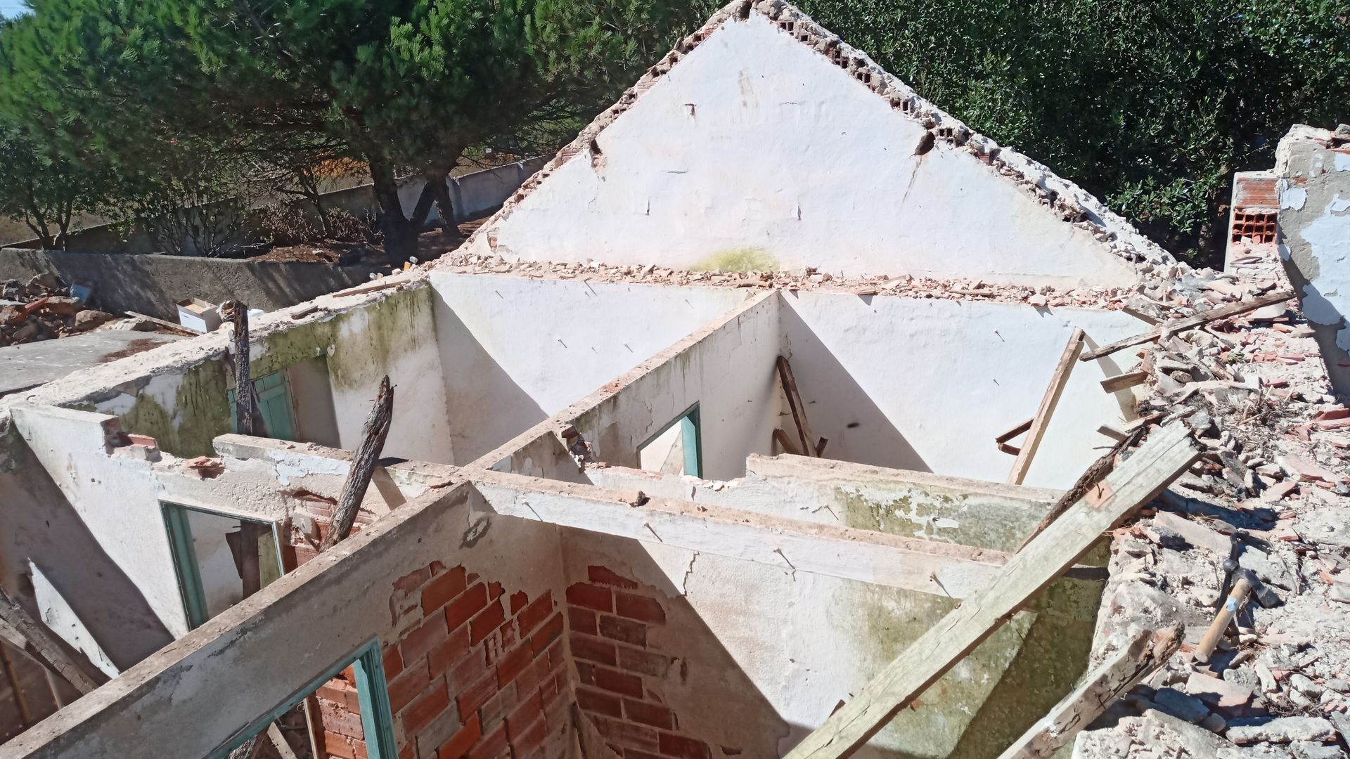 Prédio demolido com tijolos e concreto aparentes, árvores ao fundo.