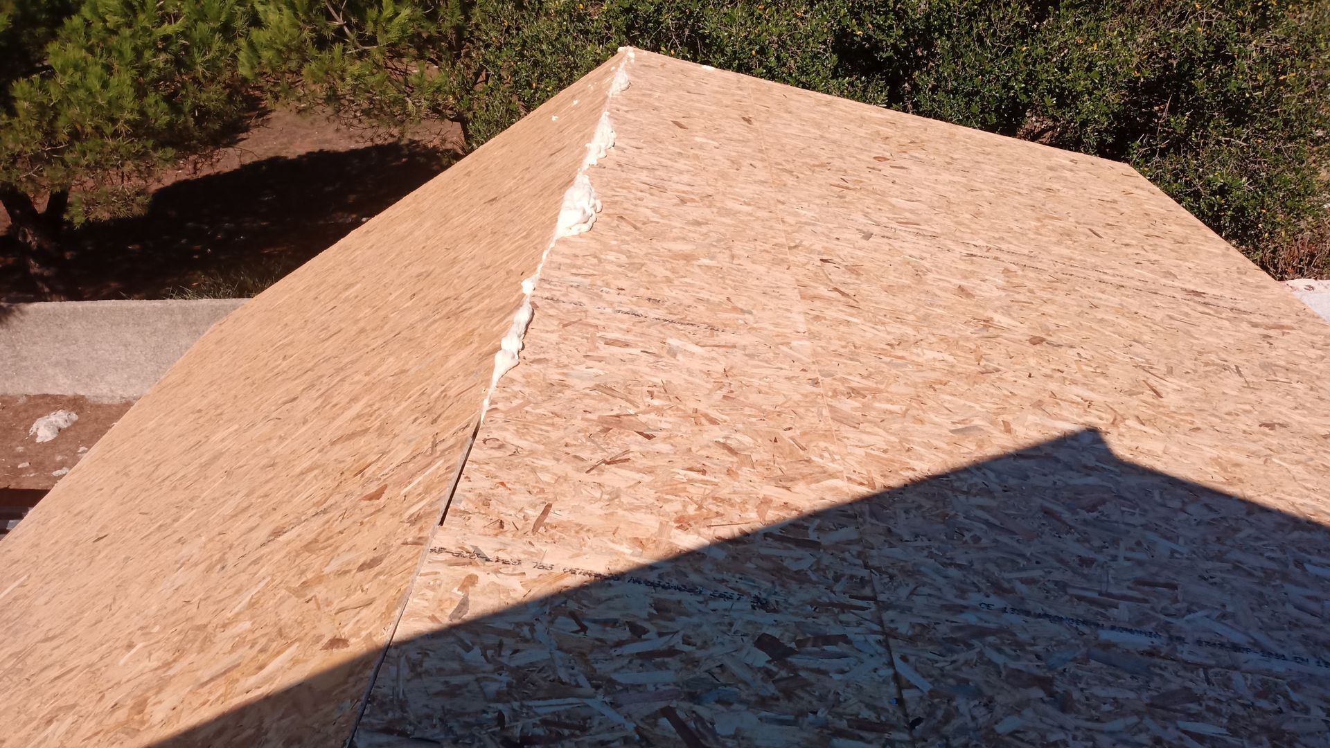 Vista aérea de um telhado parcialmente construído com painéis de OSB (painel de madeira orientada) marrom-claro.