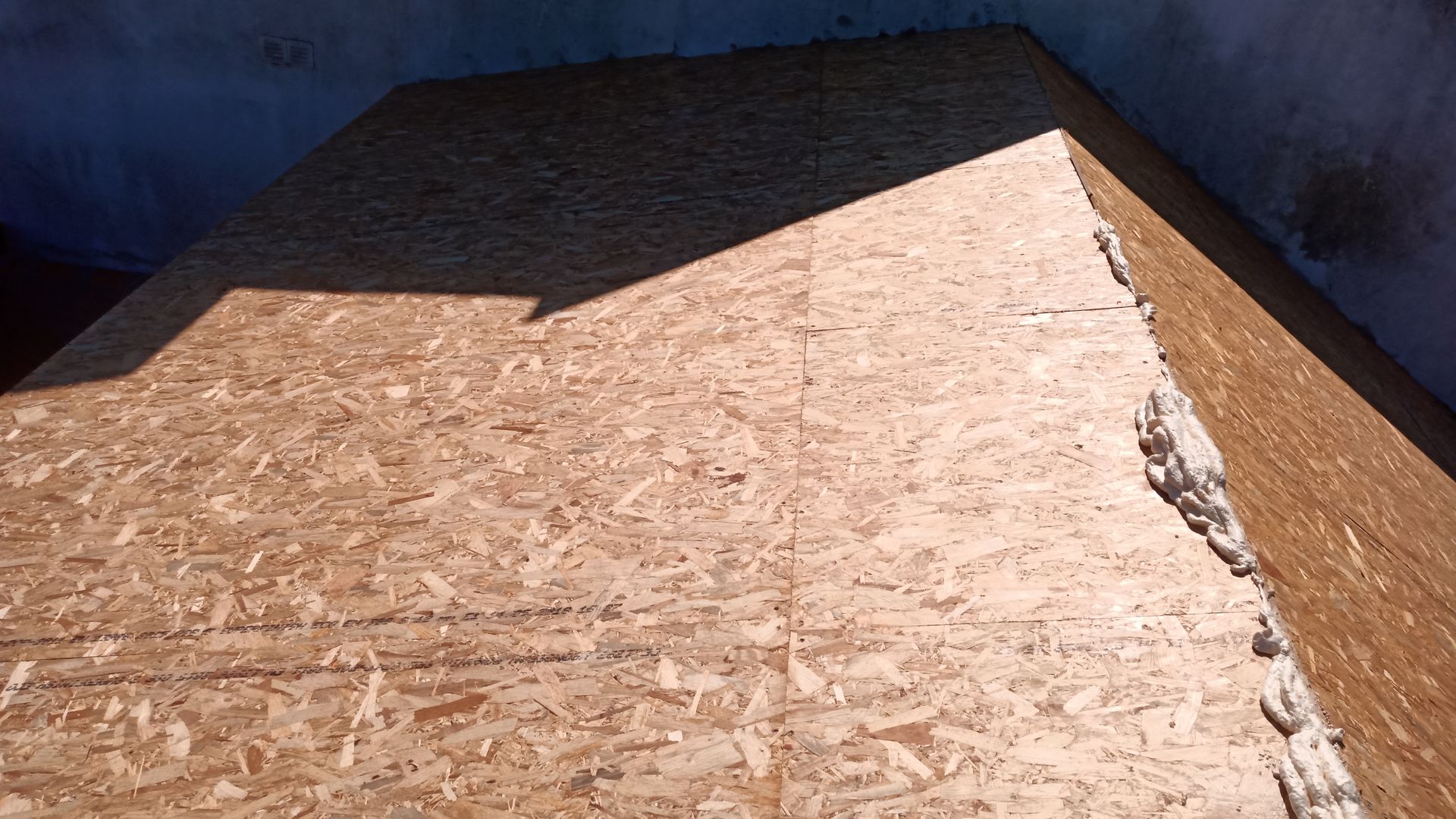 Detalhe de uma estrutura revestida de madeira compensada, com uma seção sombreada e bordas expostas.