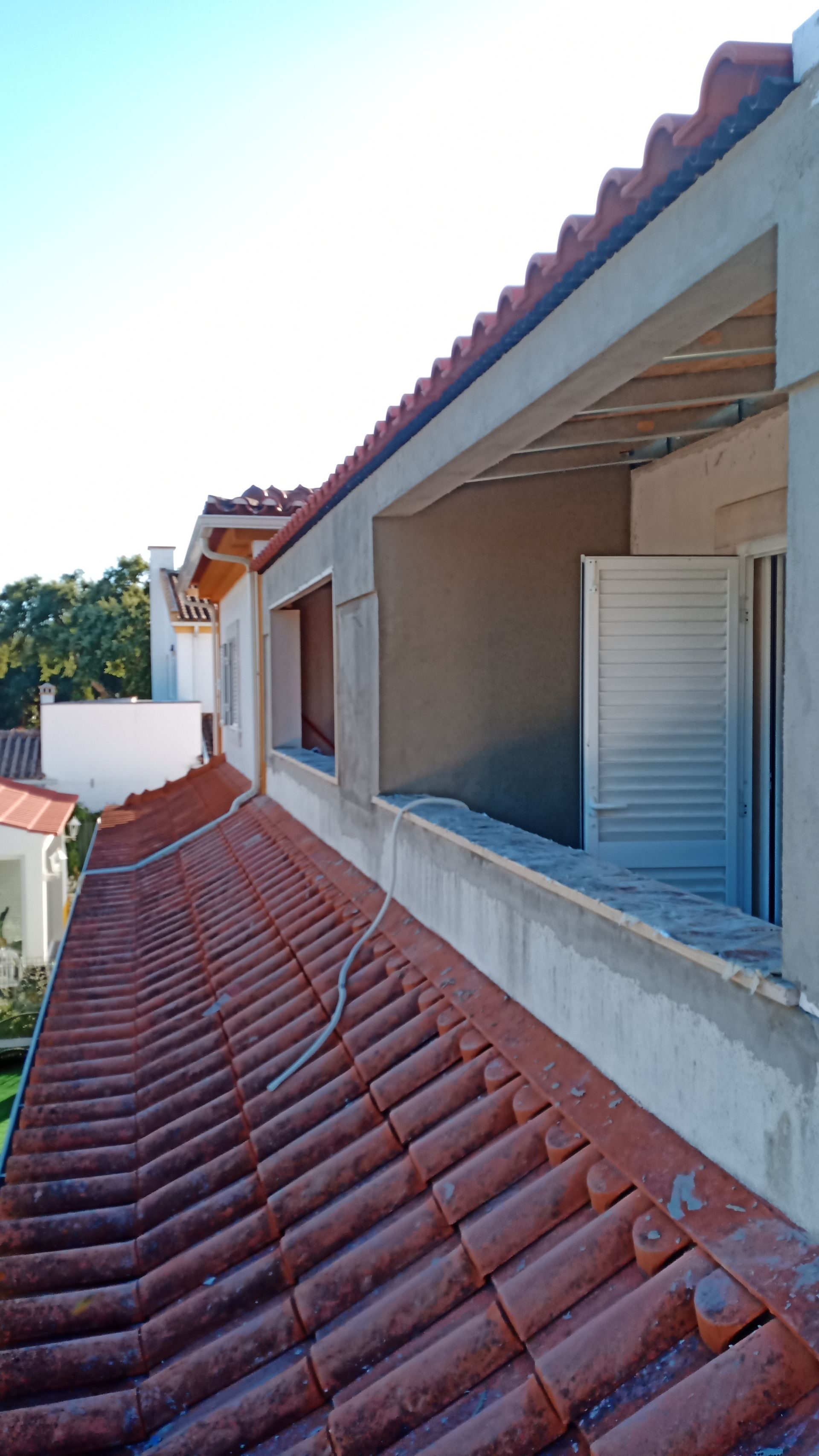 Telhado de telha vermelha com caixilho de janela inacabado e porta veneziana branca.