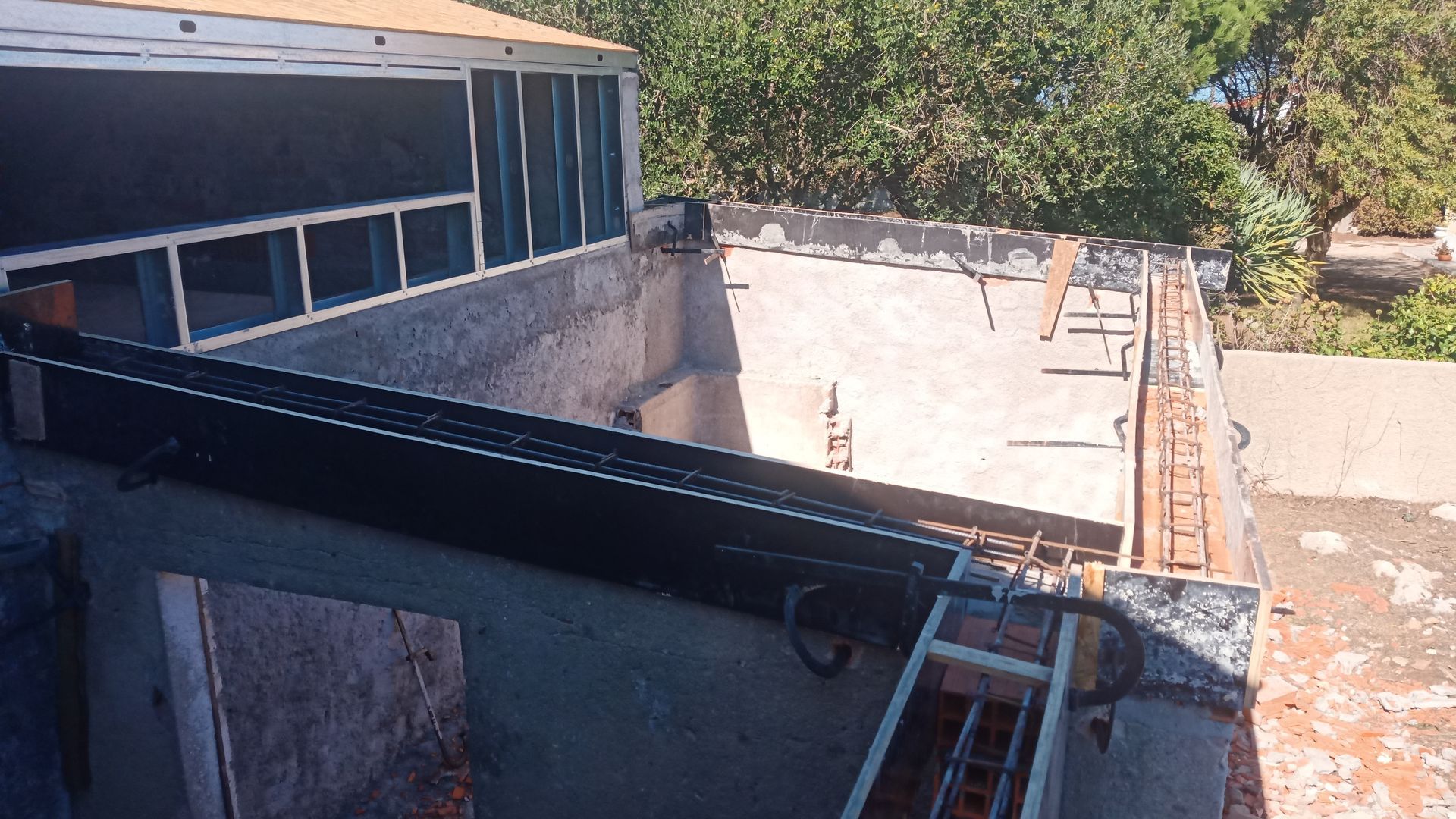 Canteiro de obras: estrutura parcialmente construída com vergalhões expostos e uma calha preta; escada visível.