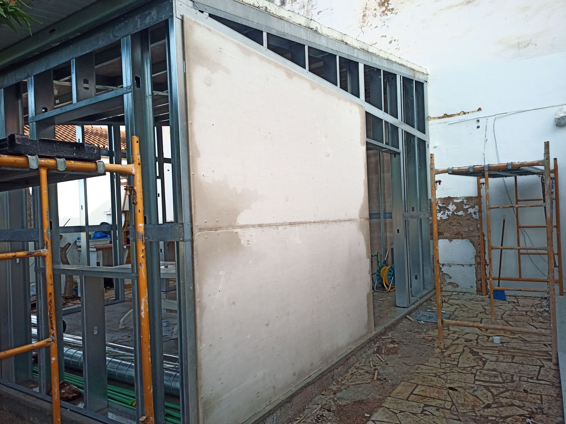 Estrutura metálica com drywall parcialmente instalado, em um canteiro de obras.