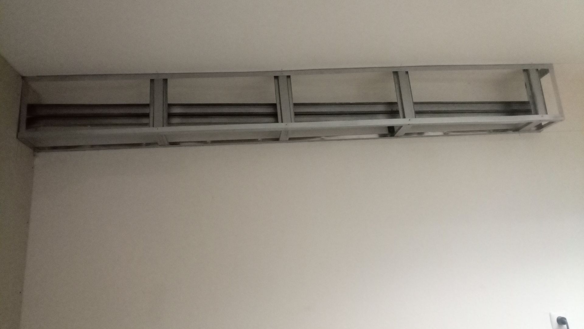 Estrutura metálica fixada em uma parede branca, possivelmente para prateleiras ou um armário.