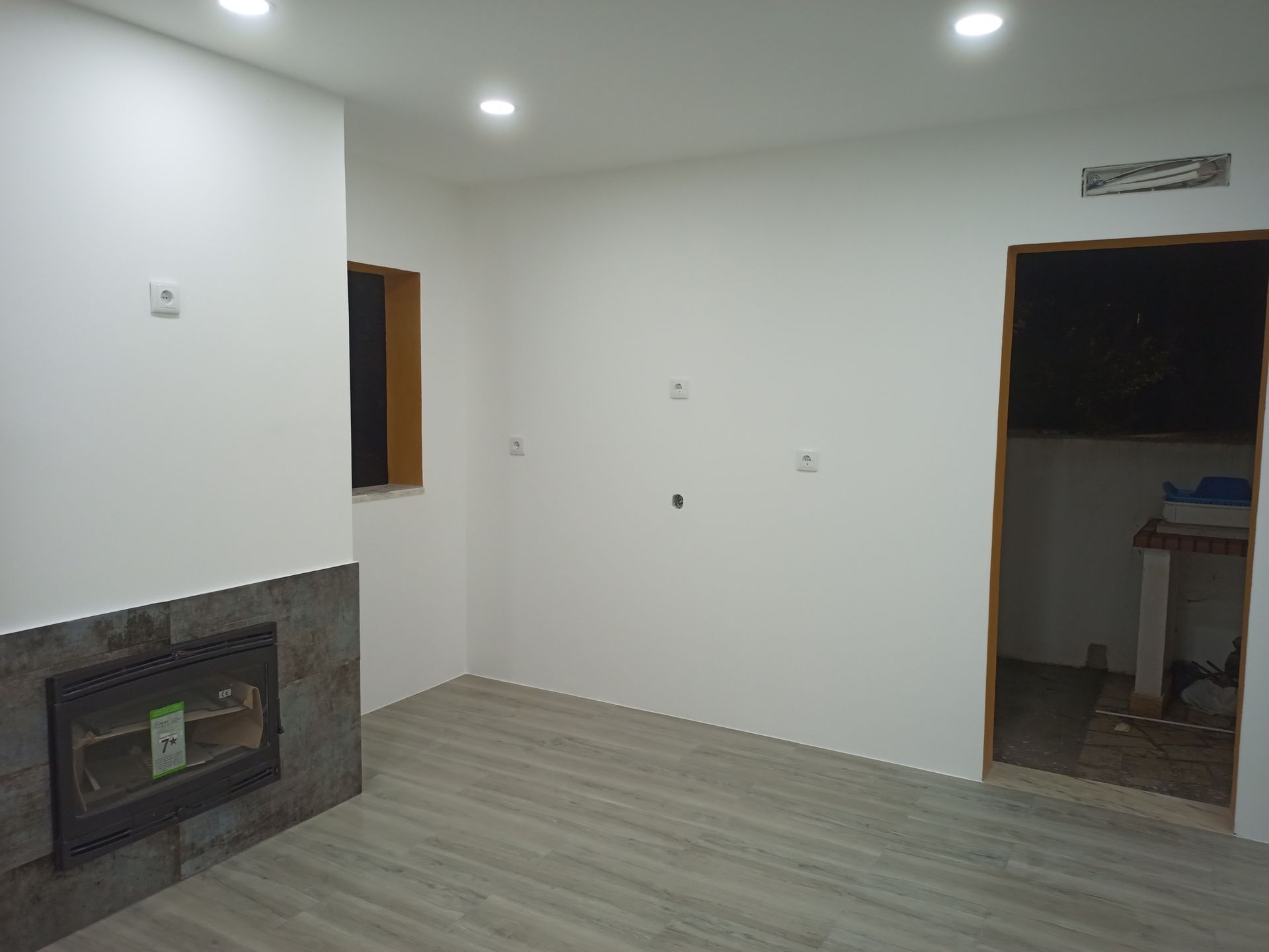 Sala branca vazia com lareira, piso cinza e uma porta.