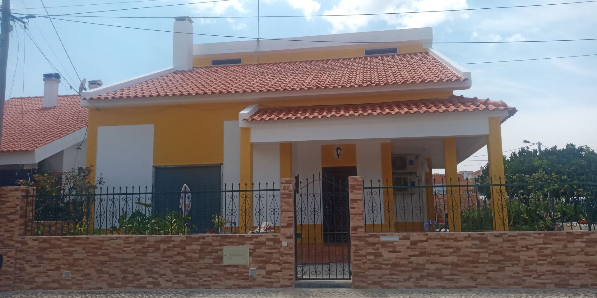 Casa amarela com telhado de telhas laranja, varanda e portão de ferro preto.