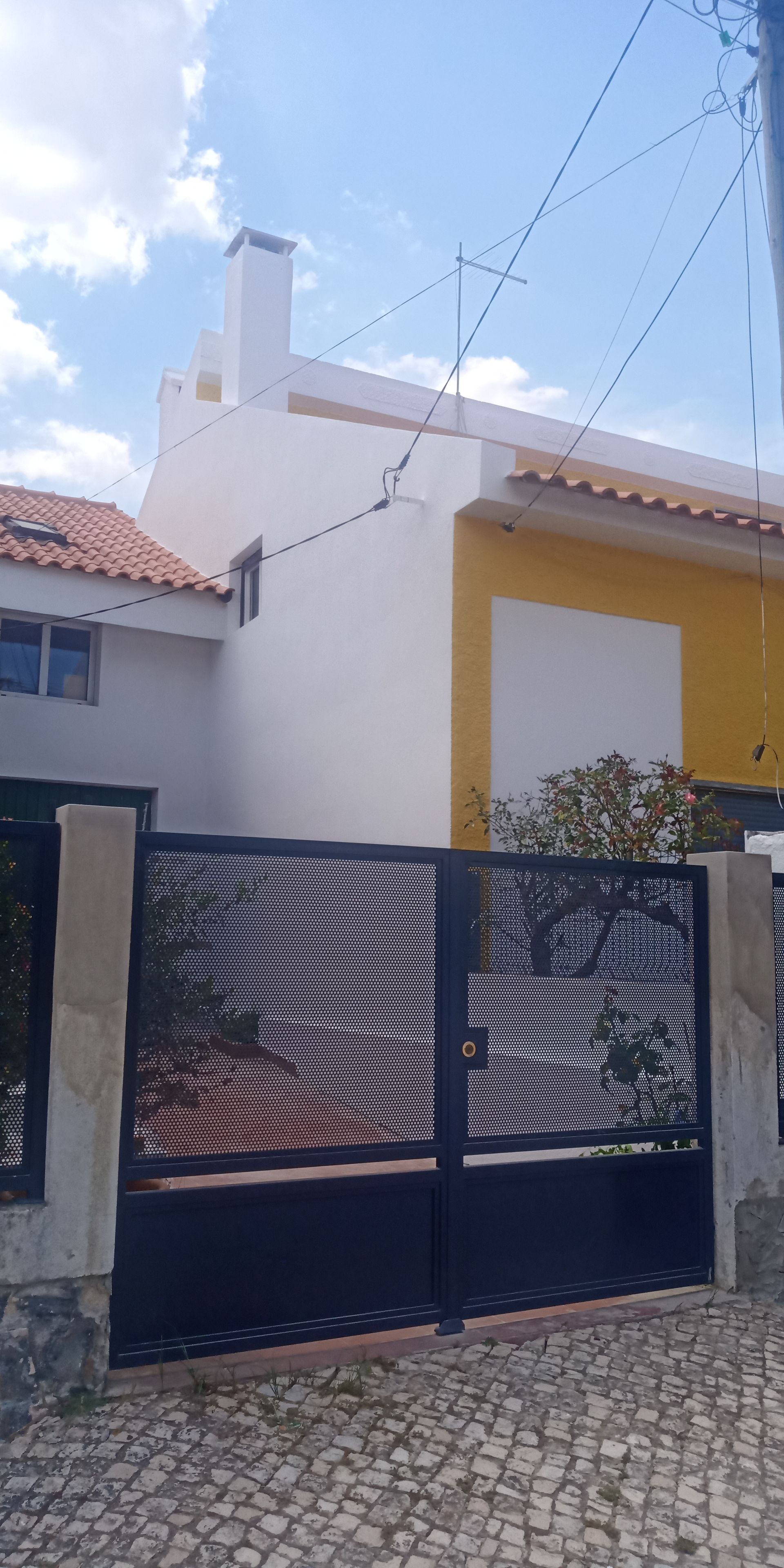 Uma casa com um portão preto, paredes amarelas e brancas e um céu azul.