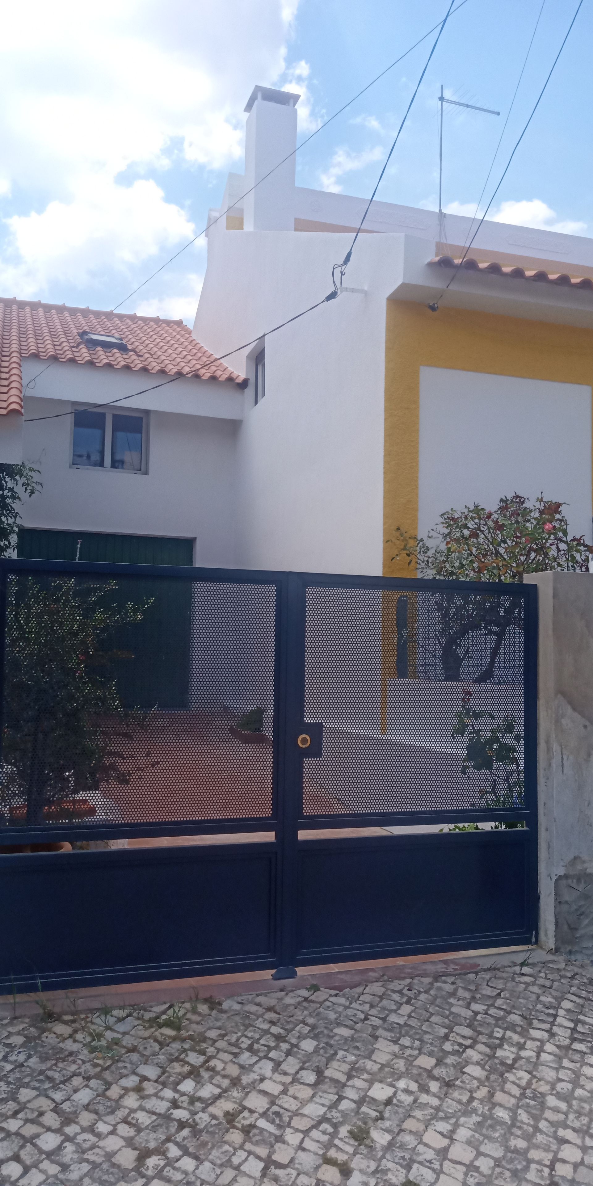 Portão preto em frente a um prédio branco com telhado de telhas vermelhas e detalhes em amarelo.