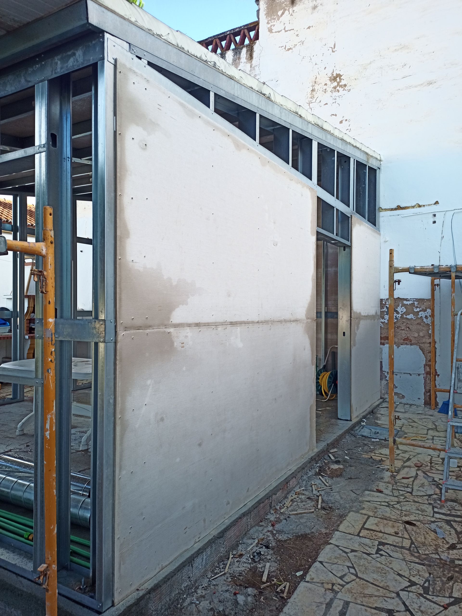Canteiro de obras: parede com estrutura metálica com drywall e gesso parcialmente instalados.
