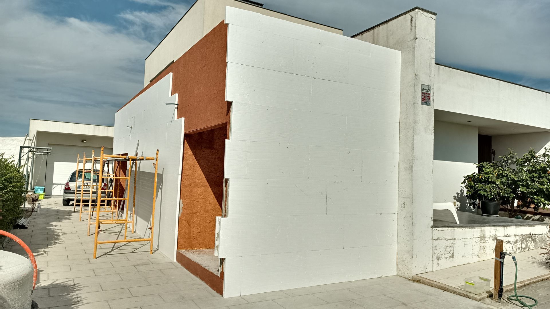 Exterior da casa em construção; painéis de isolamento de espuma branca fixados na lateral, andaime na frente.