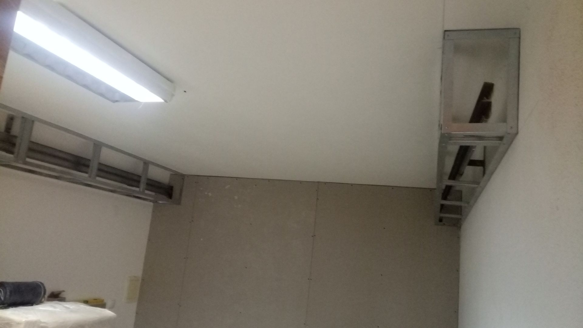 Estrutura metálica parcialmente instalada na parede e no teto; luminária fluorescente.