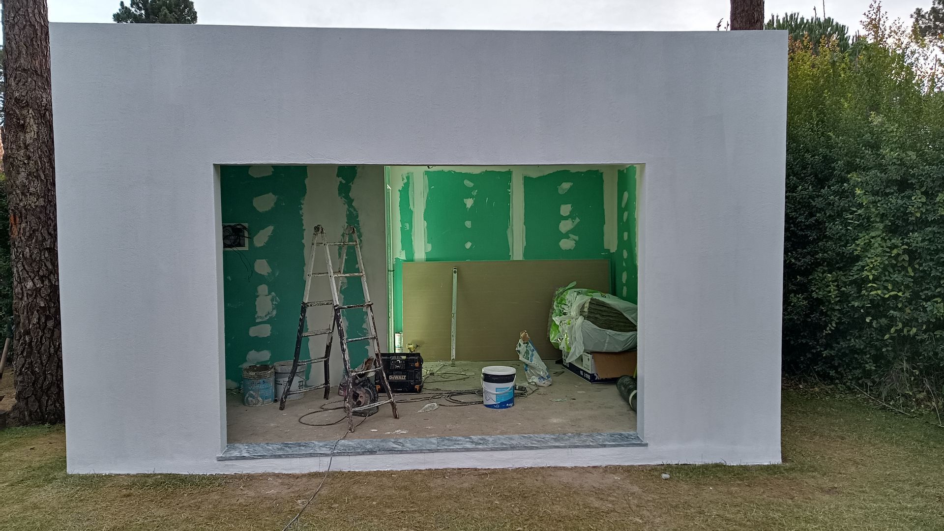 Exterior de uma estrutura em construção; exterior branco, interior verde, ferramentas e materiais dentro da abertura.