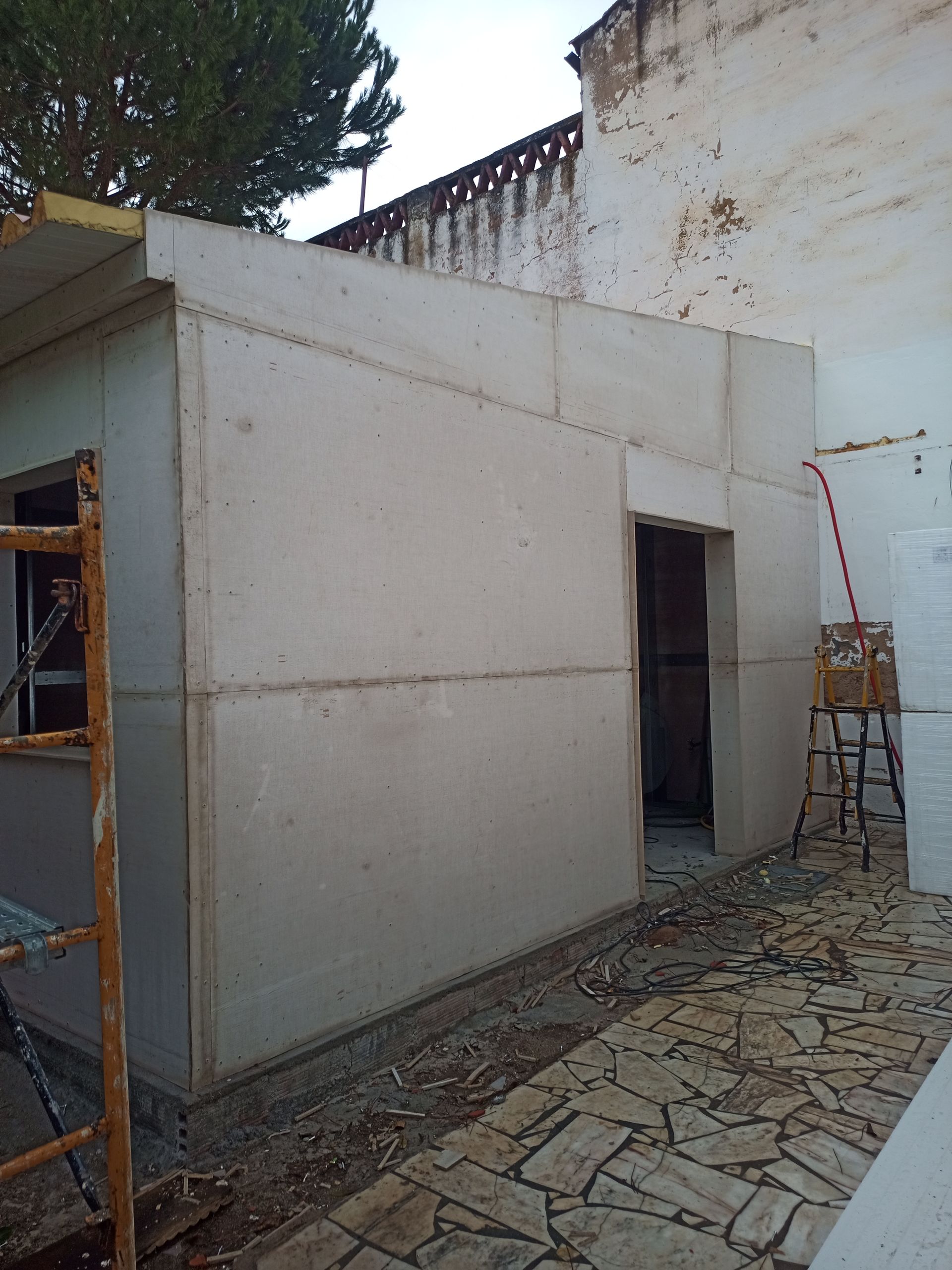 Vista exterior de um edifício em construção, apresentando paredes de concreto, uma moldura de porta e uma abertura de janela.