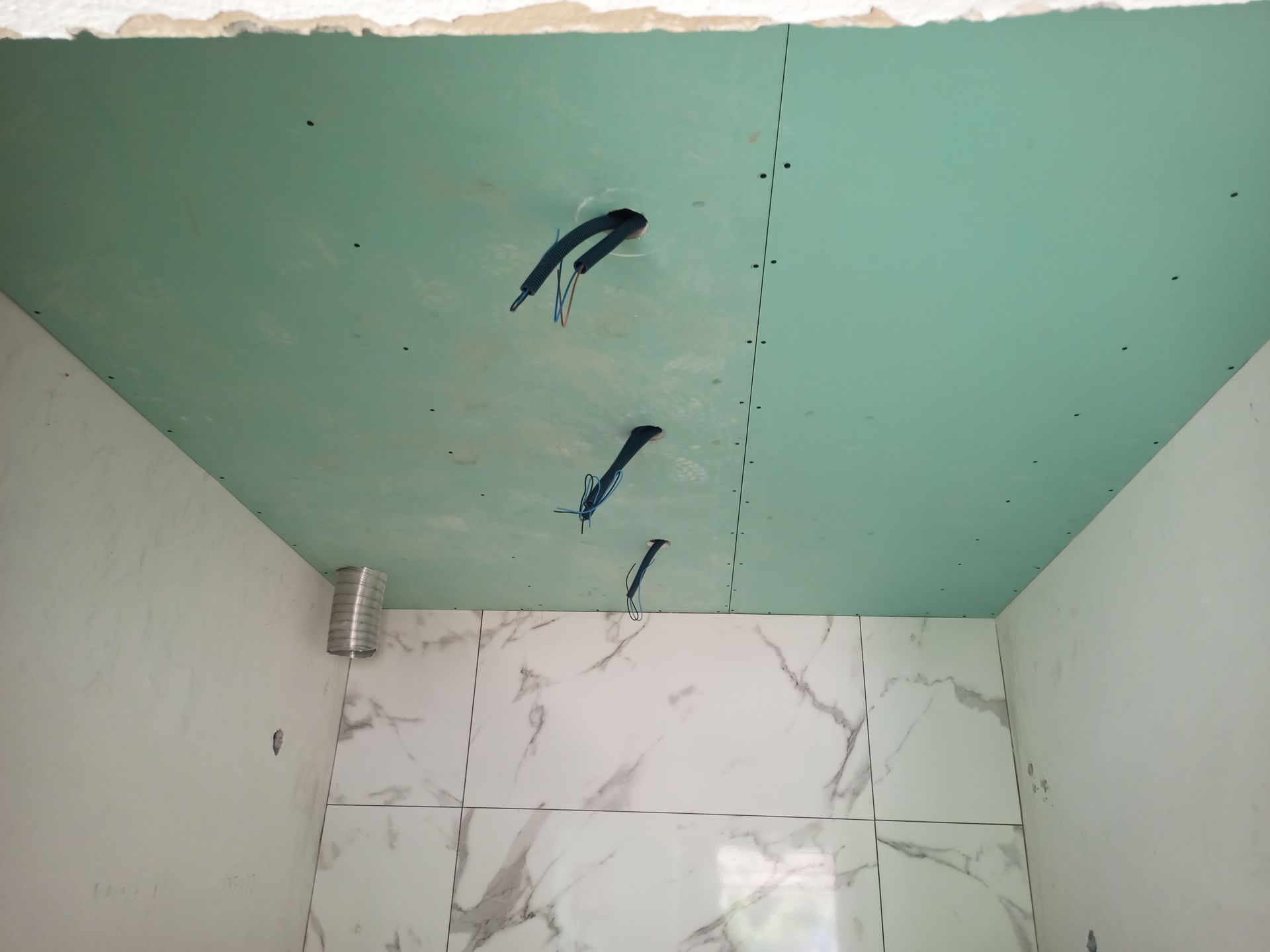 Teto de gesso cartonado verde com fios elétricos expostos; paredes revestidas com azulejos abaixo.