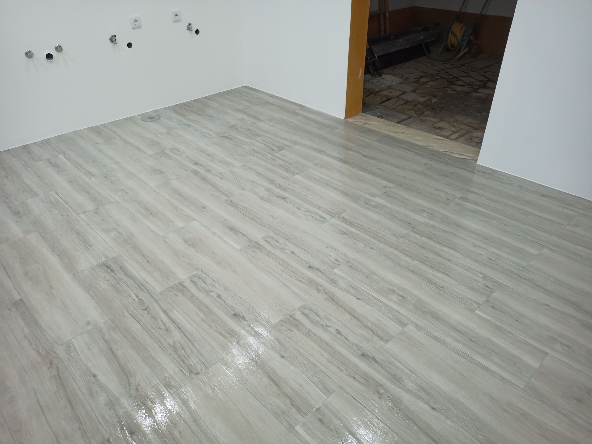 Piso cerâmico imitando madeira em tom claro, recém-instalado em um cômodo com paredes brancas e uma porta de entrada.