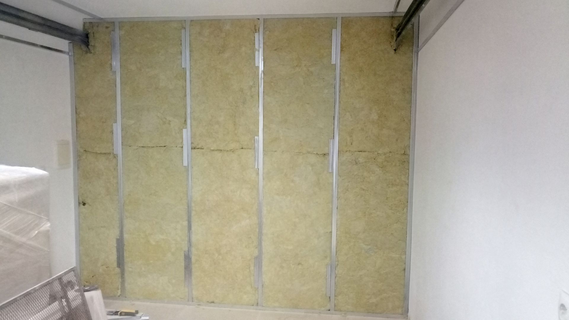 Construção de parede interna. Painéis de isolamento vertical instalados com estrutura metálica. Bege e branco.
