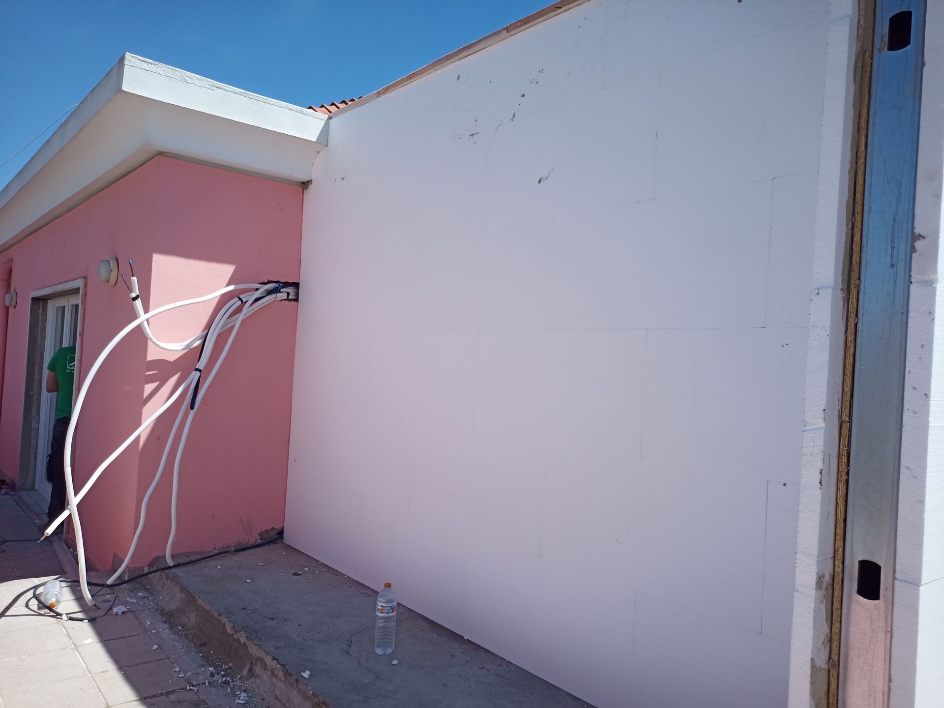 Exterior de um edifício com paredes cor-de-rosa, tubagens brancas e uma parede branca inacabada.