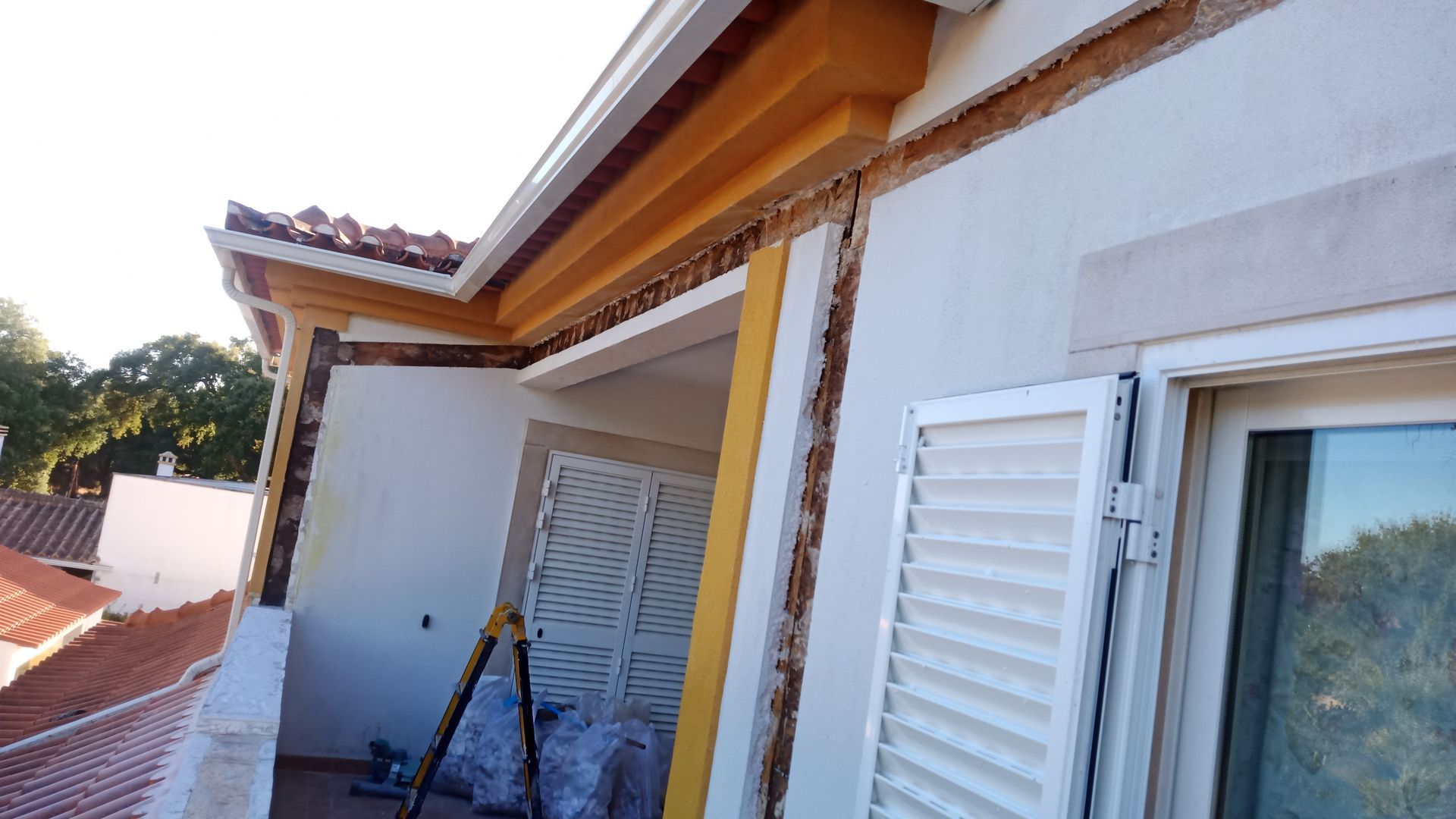 Edifício em reforma com fachada de madeira aparente, paredes brancas e detalhes em amarelo.