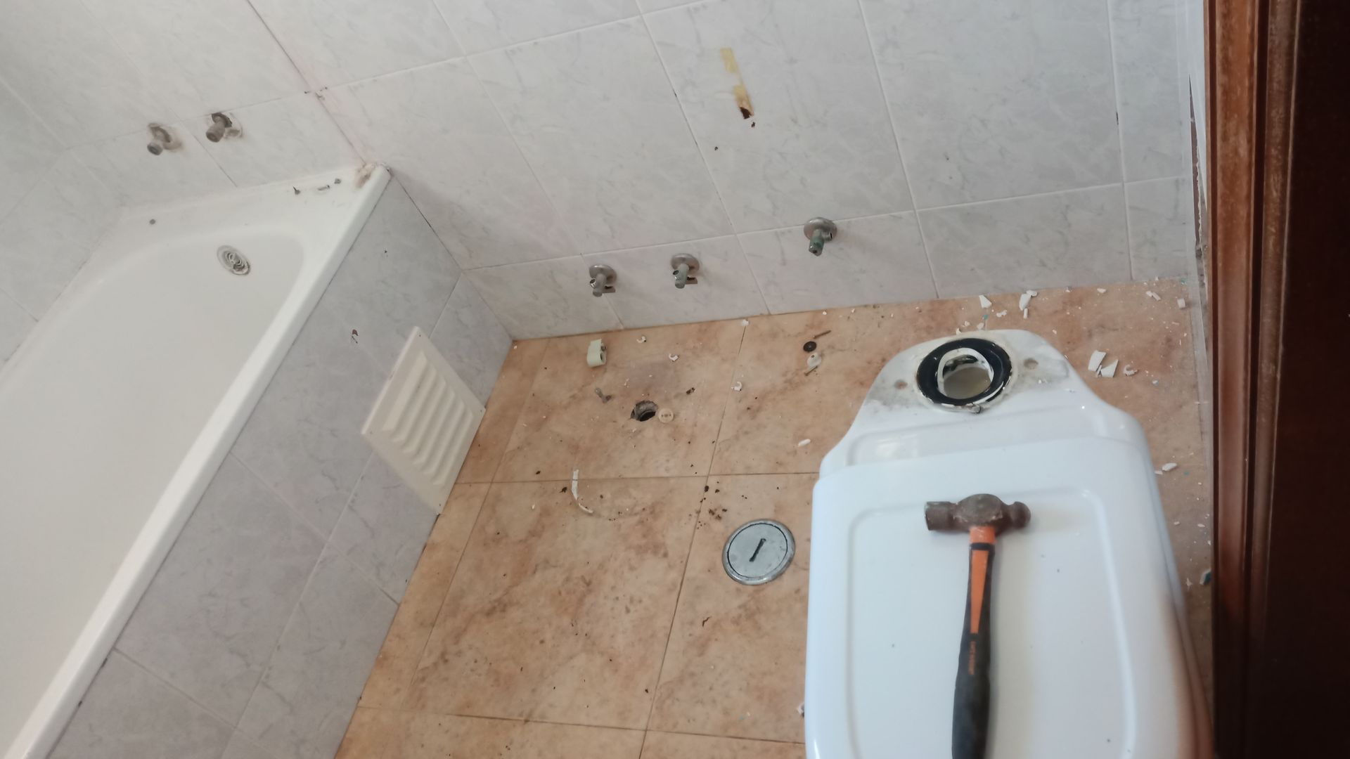 Reforma do banheiro: banheira, paredes revestidas com azulejos, vaso sanitário removido, base do vaso fixada com martelo.