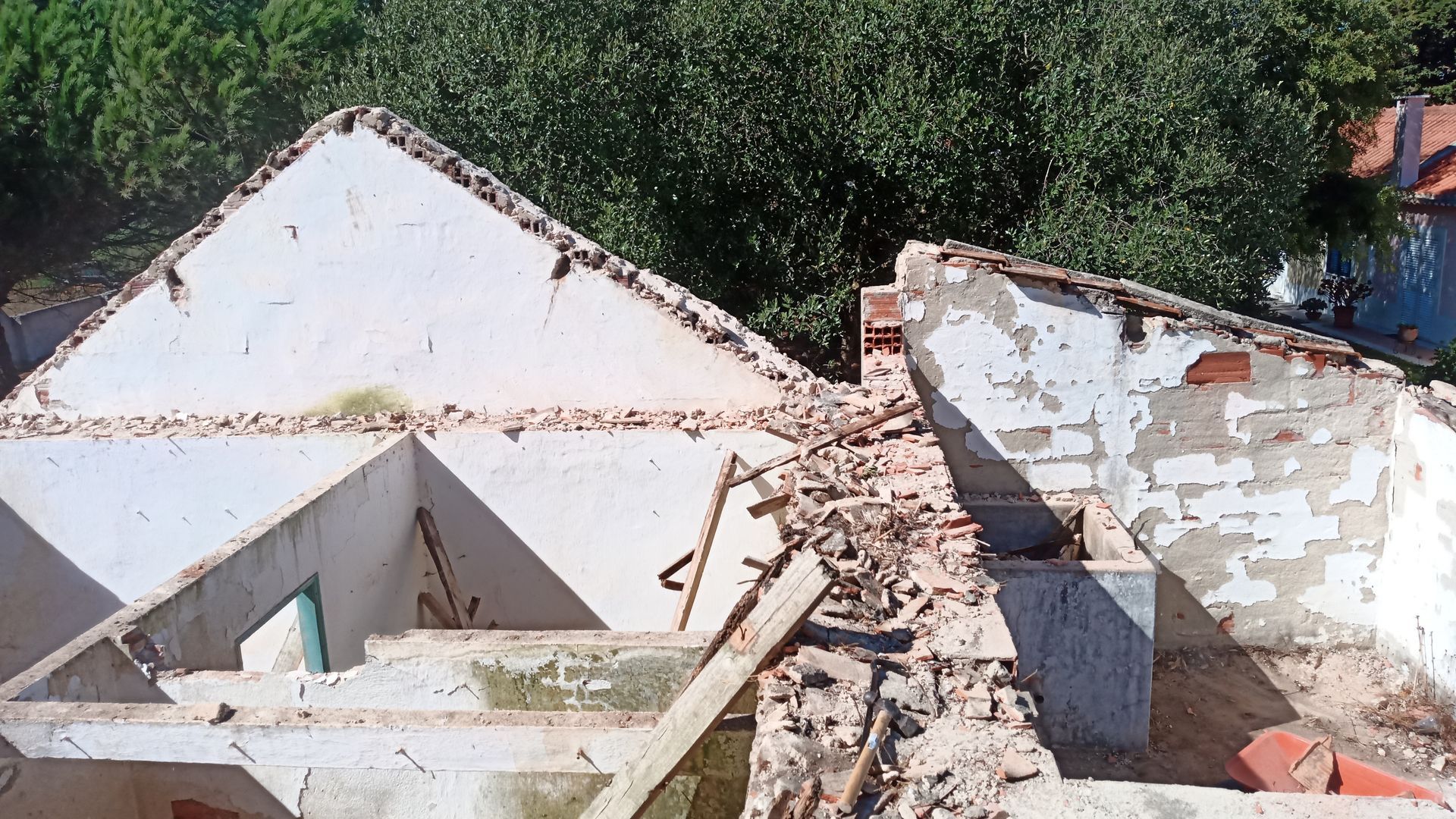 Detritos de um prédio de tijolos brancos; um telhado dilapidado contra árvores verdes.