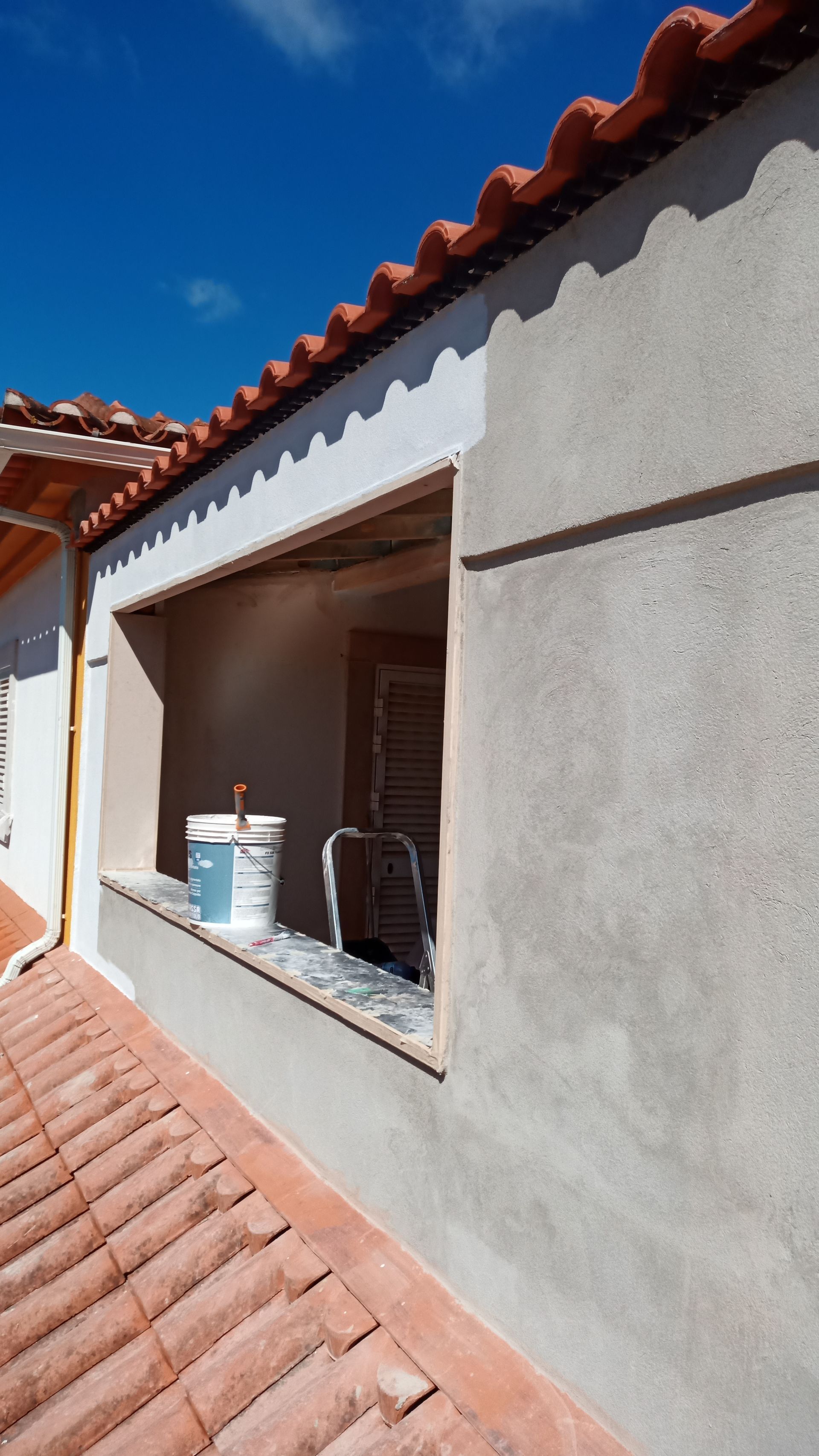 Exterior de um edifício com janela, telhas de terracota e paredes de estuque. Uma lata de tinta está no parapeito da janela.