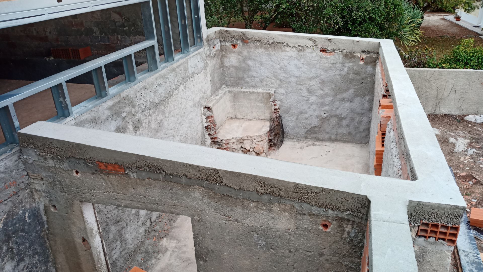 Estrutura de concreto e tijolo em construção, com estrutura aparente e exterior circundante.