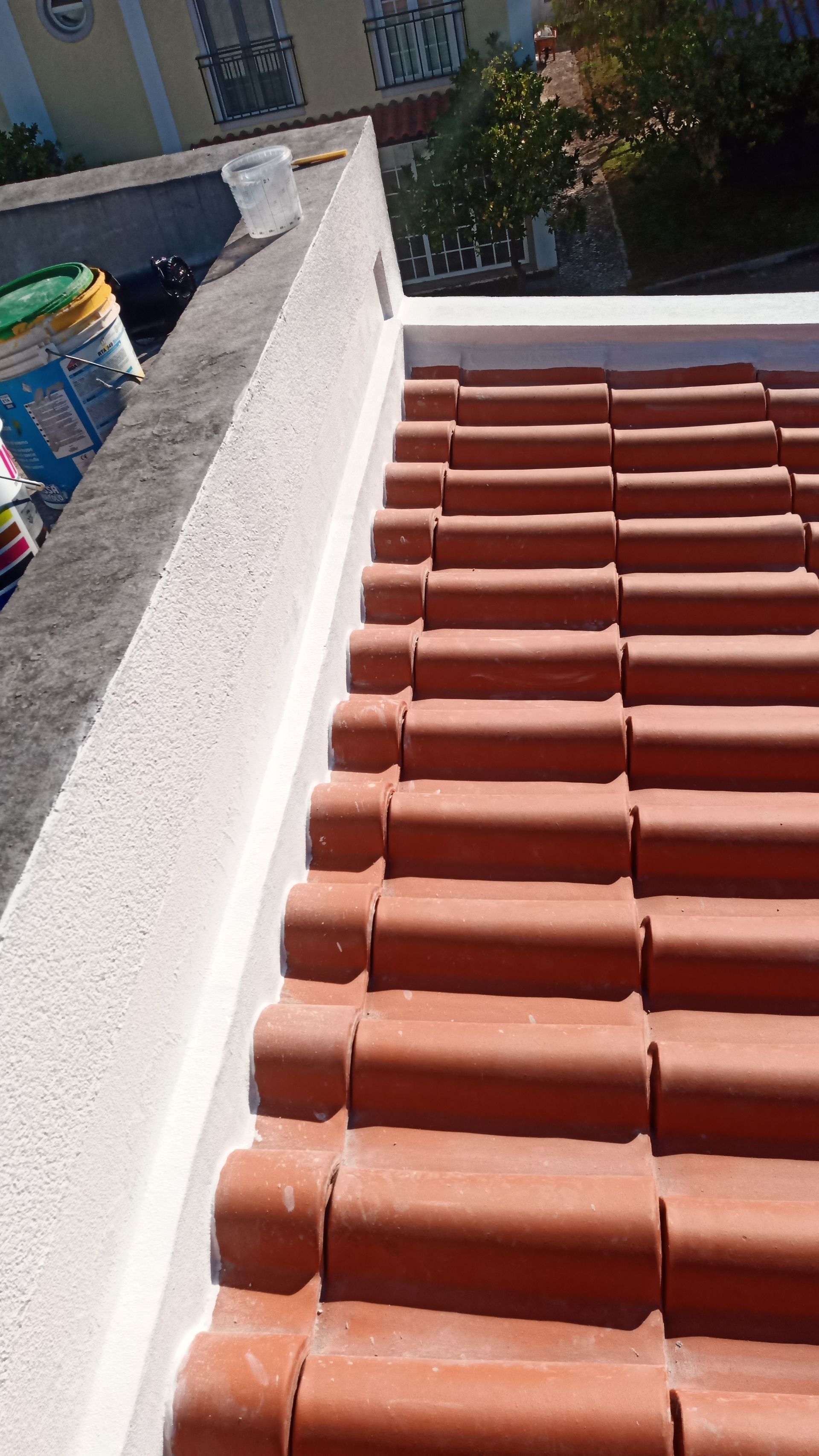 Telhado de telha vermelha ao lado de uma parede de estuque branco; vista de cima.