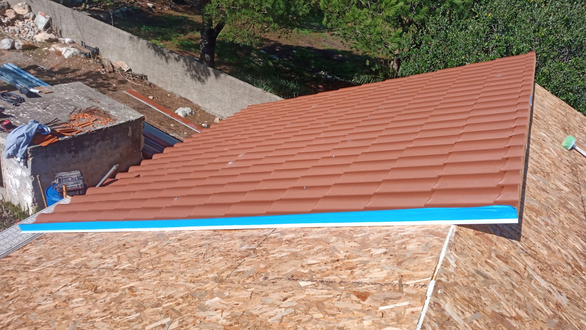 Telhado parcialmente coberto com telhas marrons e detalhes em azul, em ambiente externo.