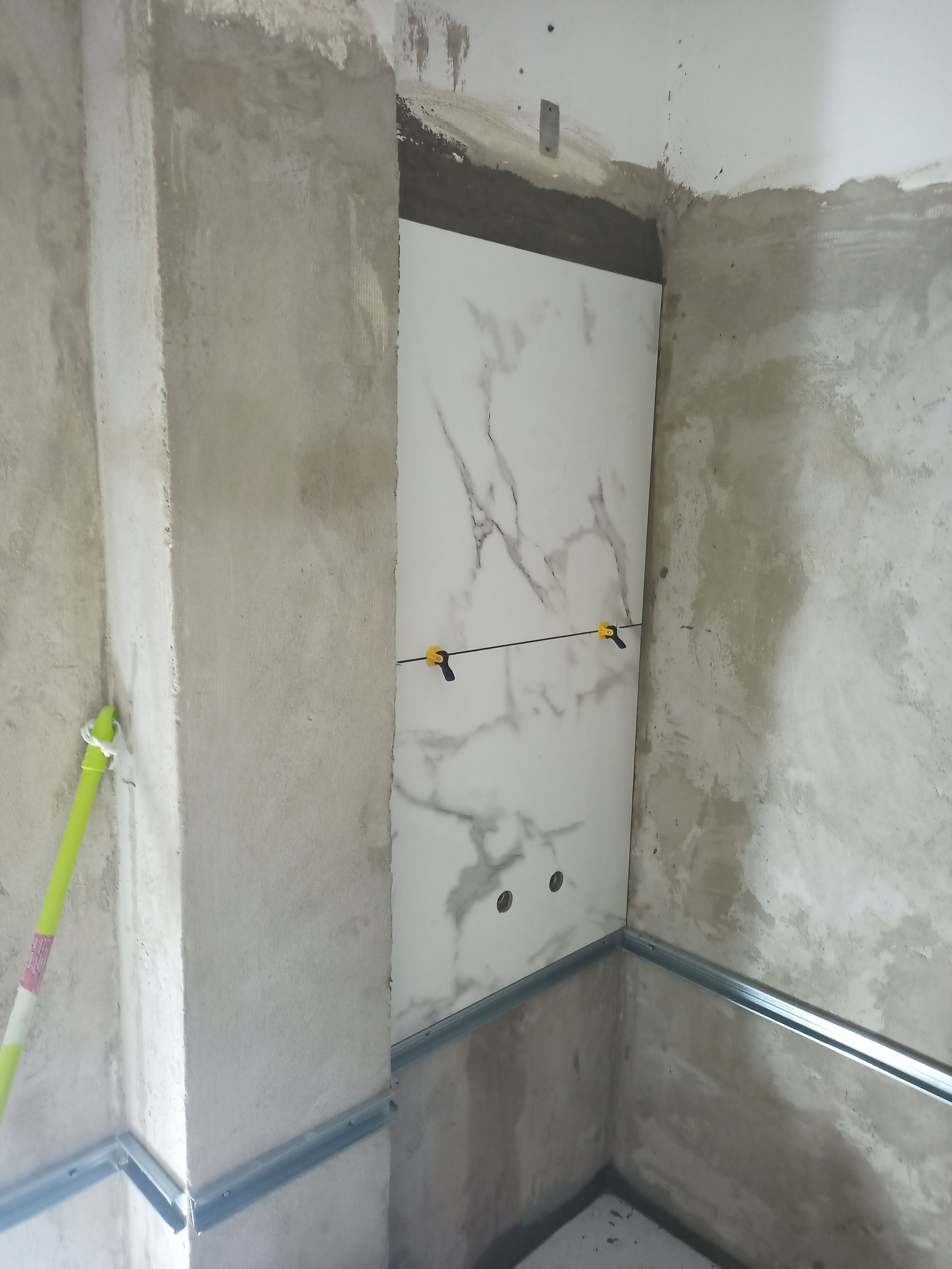 Um azulejo com aparência de mármore está embutido em um nicho na parede com borda metálica. Materiais de construção o circundam.