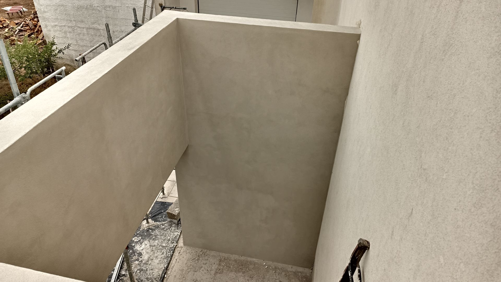 Paredes rebocadas em bege formando um canto externo; o chão coberto de entulho.