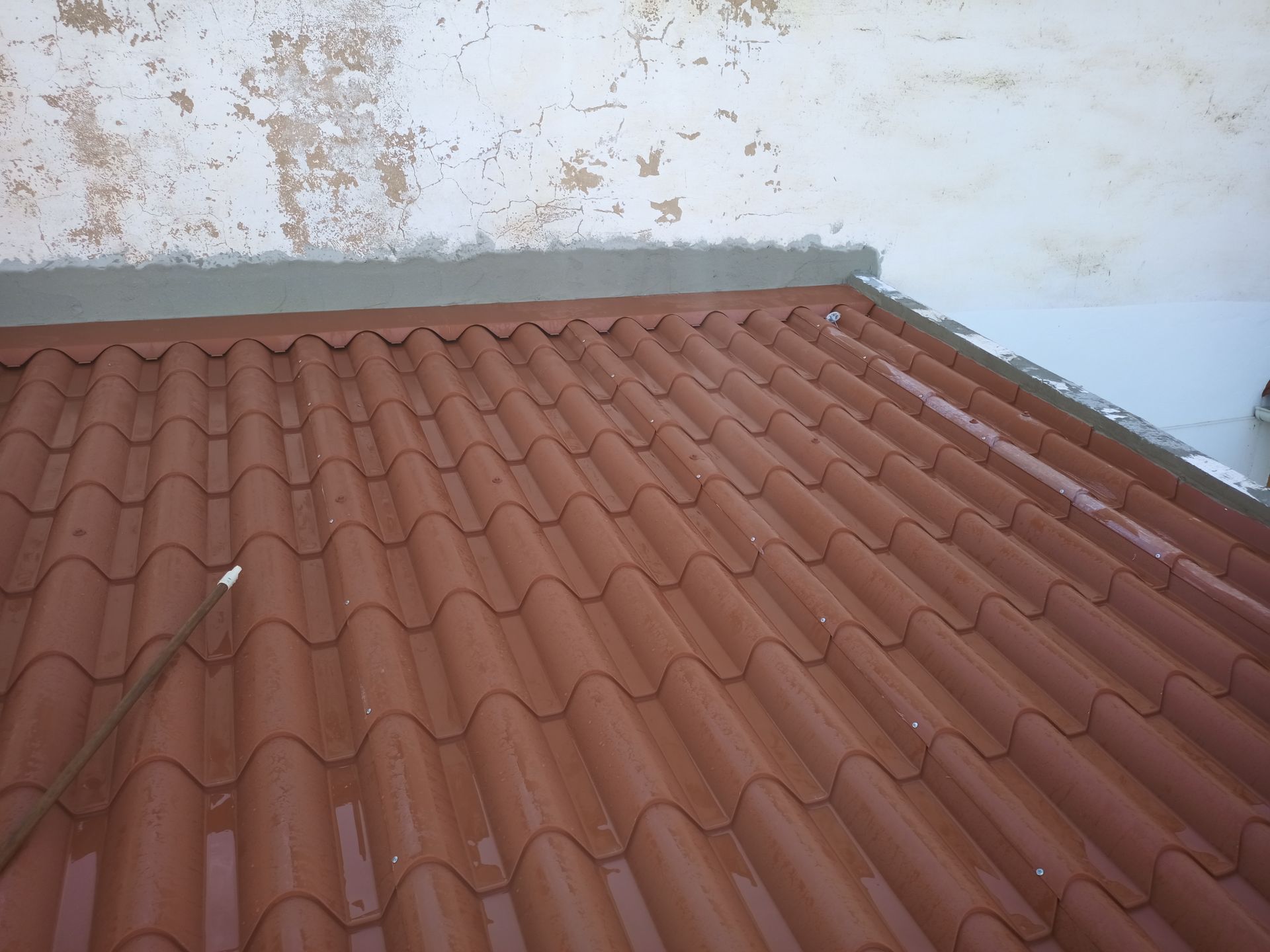 Telhado de telha vermelha encontra uma parede branca com tinta descascando; selante de cimento na junção.