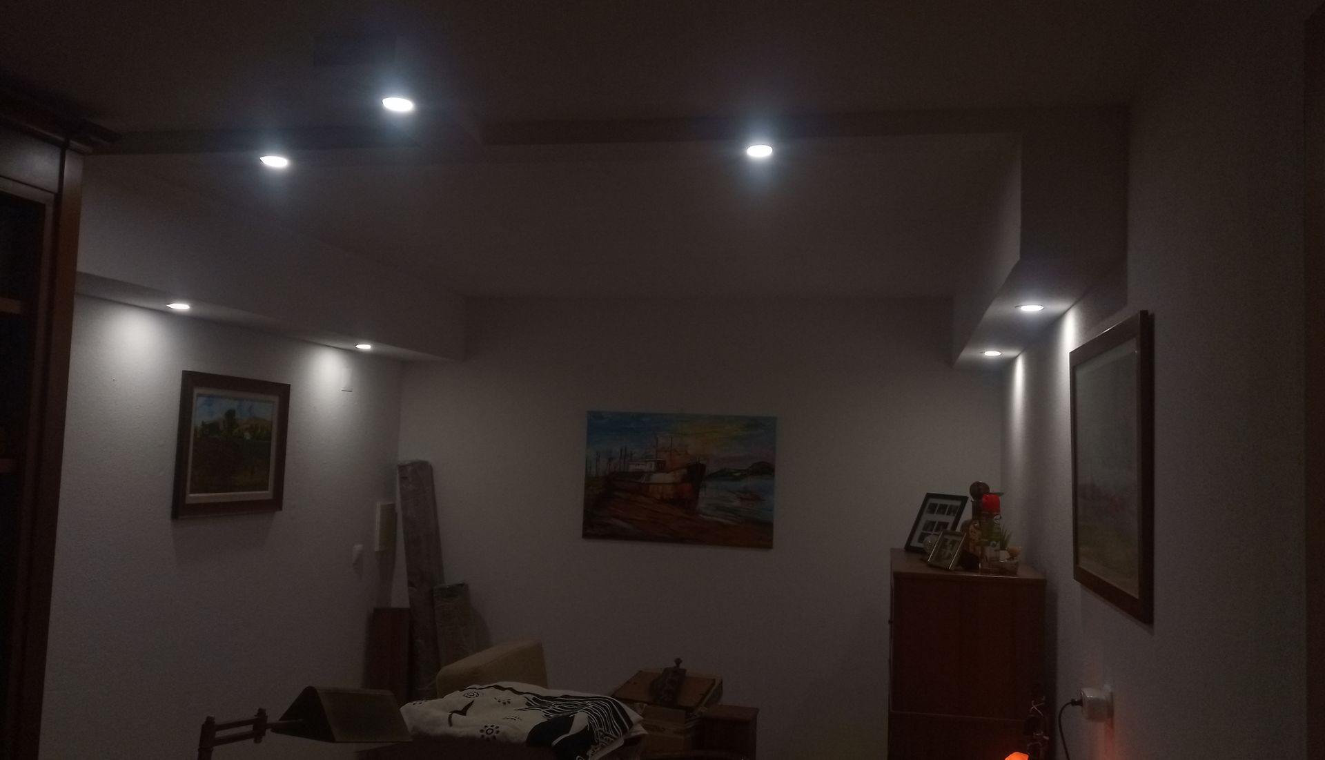 Um interior com iluminação tênue, com luzes embutidas no teto iluminando pinturas em paredes brancas.