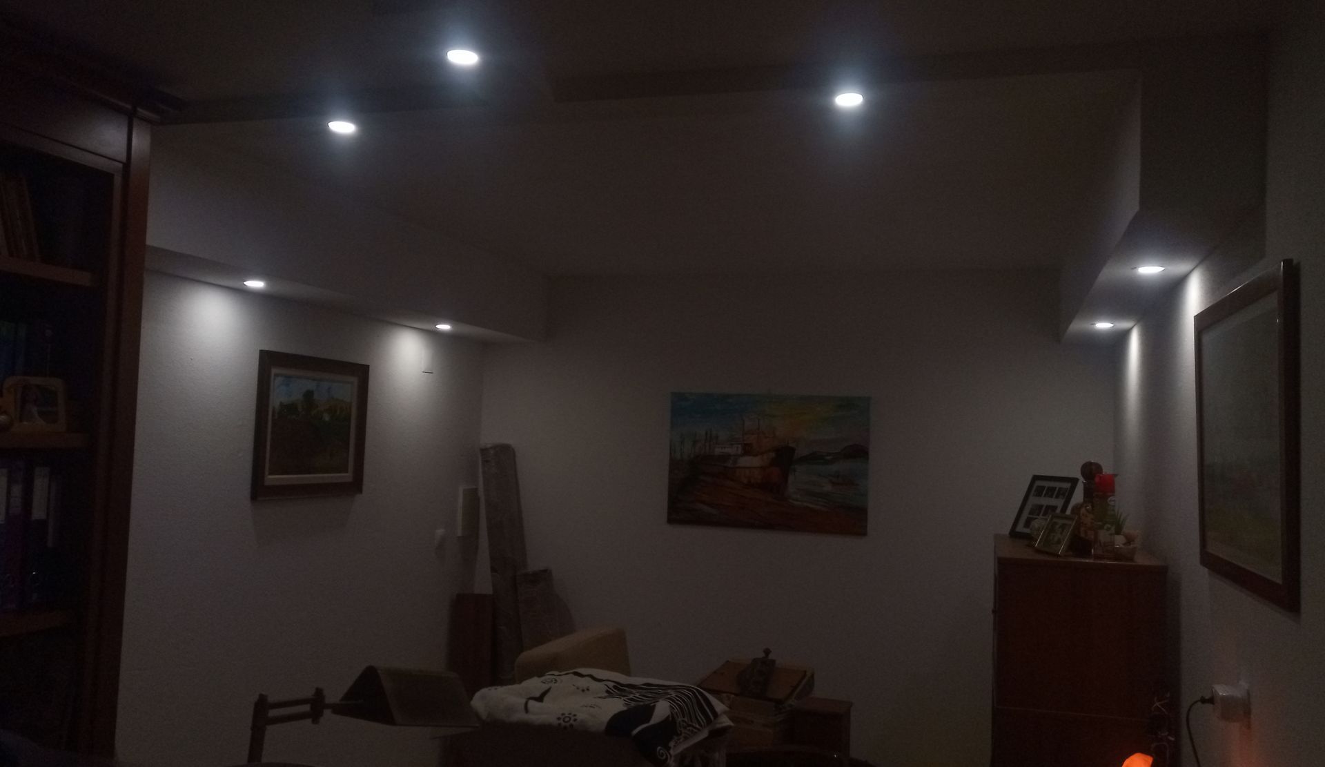 Um quarto com iluminação tênue e luzes embutidas no teto que iluminam pinturas e móveis.